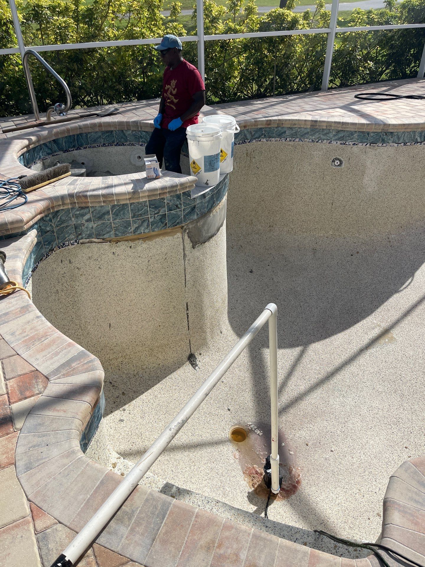 Empty drained pool with curved concrete walls and a worker standing at the edge holding supplies.