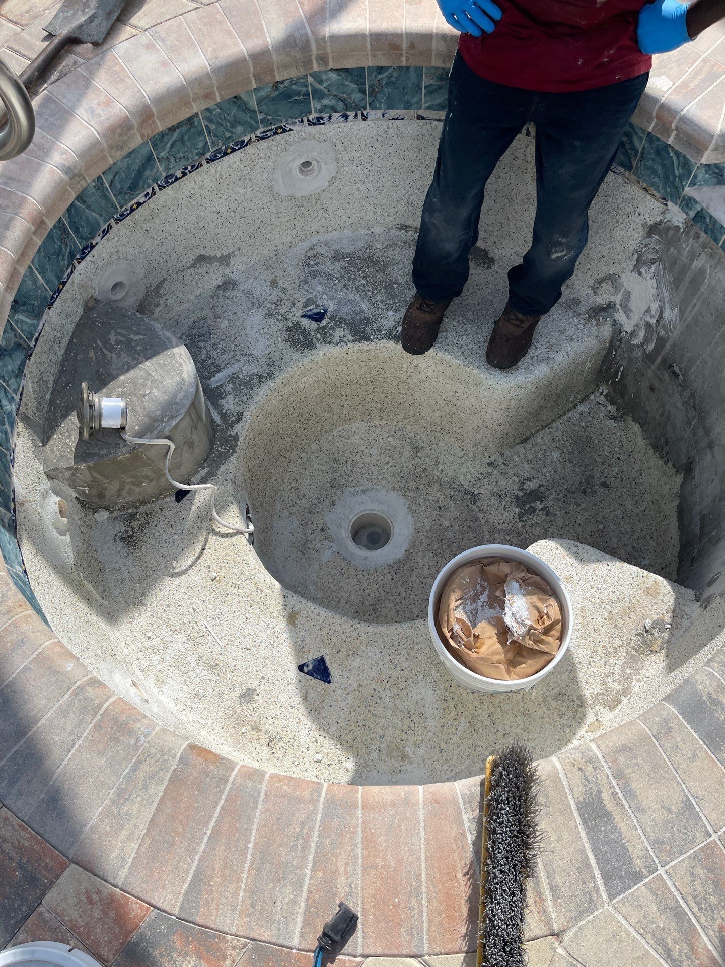 Child standing in a circular stone fountain or pit with a central drain and a small bucket of rocks.