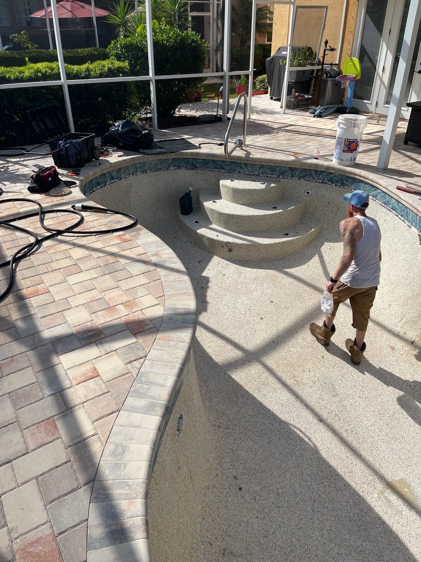Backyard patio with curved concrete seating and a worker in a blue hard hat holding a hose.