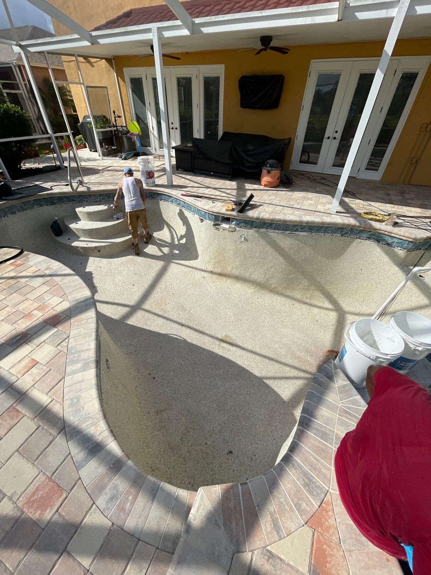 Backyard patio with a round pool, white columns, and a person standing near the pool steps.