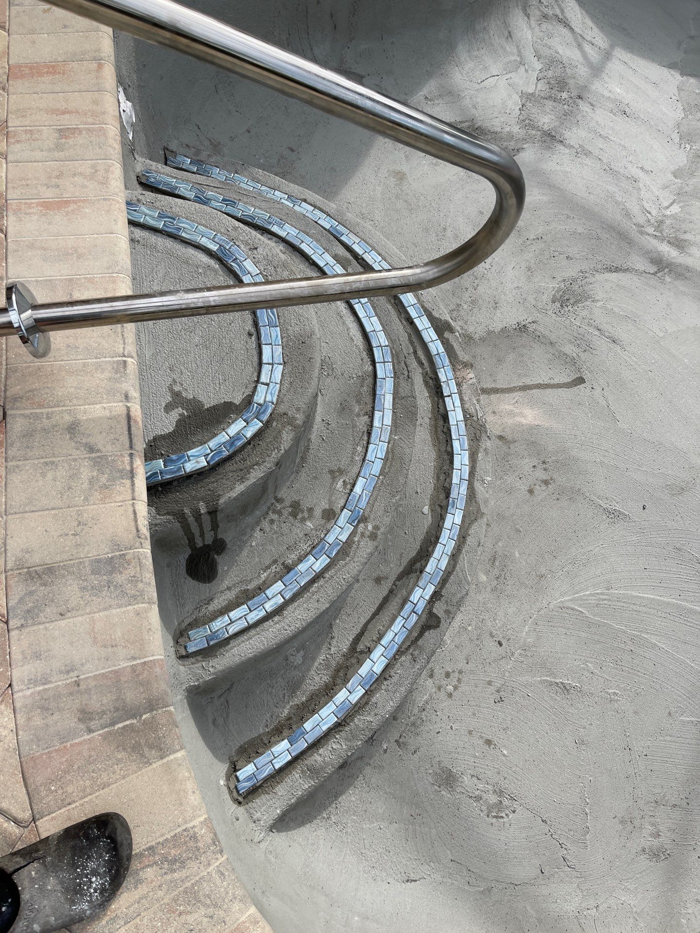 Curved concrete stairwell with metal handrail, seen from above.