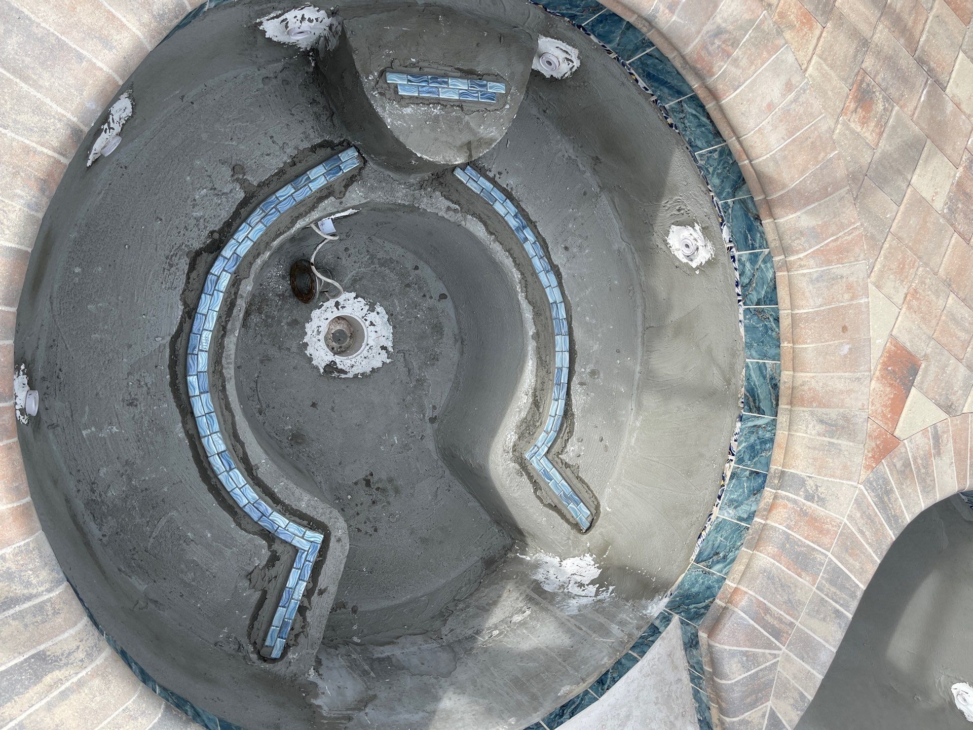 Aerial view of a circular stone fountain with blue accents and shallow water in a paved plaza.