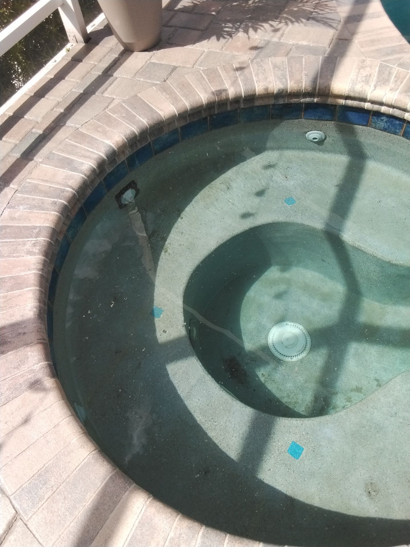 Round pool with shallow greenish water and tiled stone deck, viewed from above.