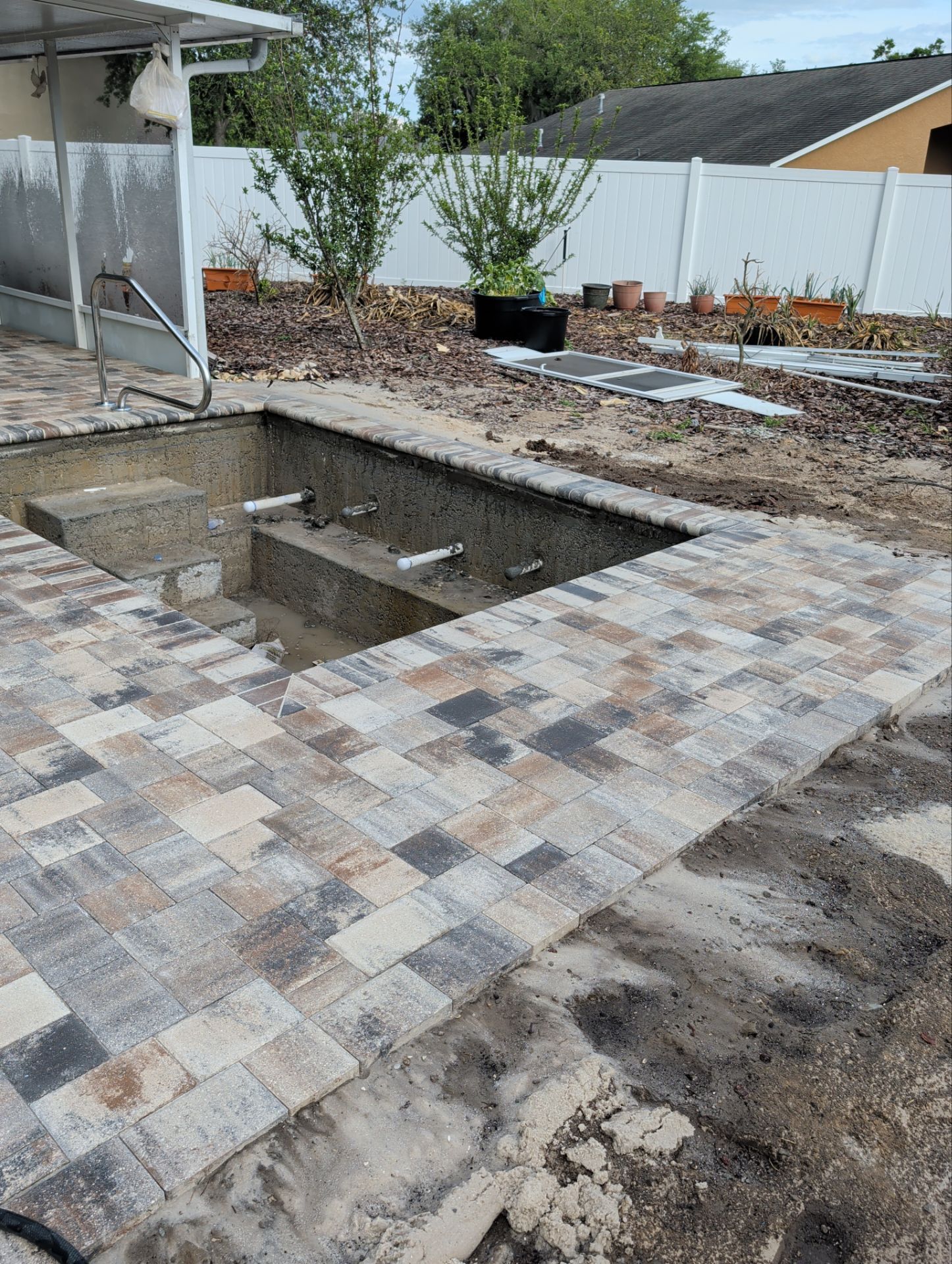 Backyard patio with an empty sunken rectangular pool area and newly laid stone pavers around it.