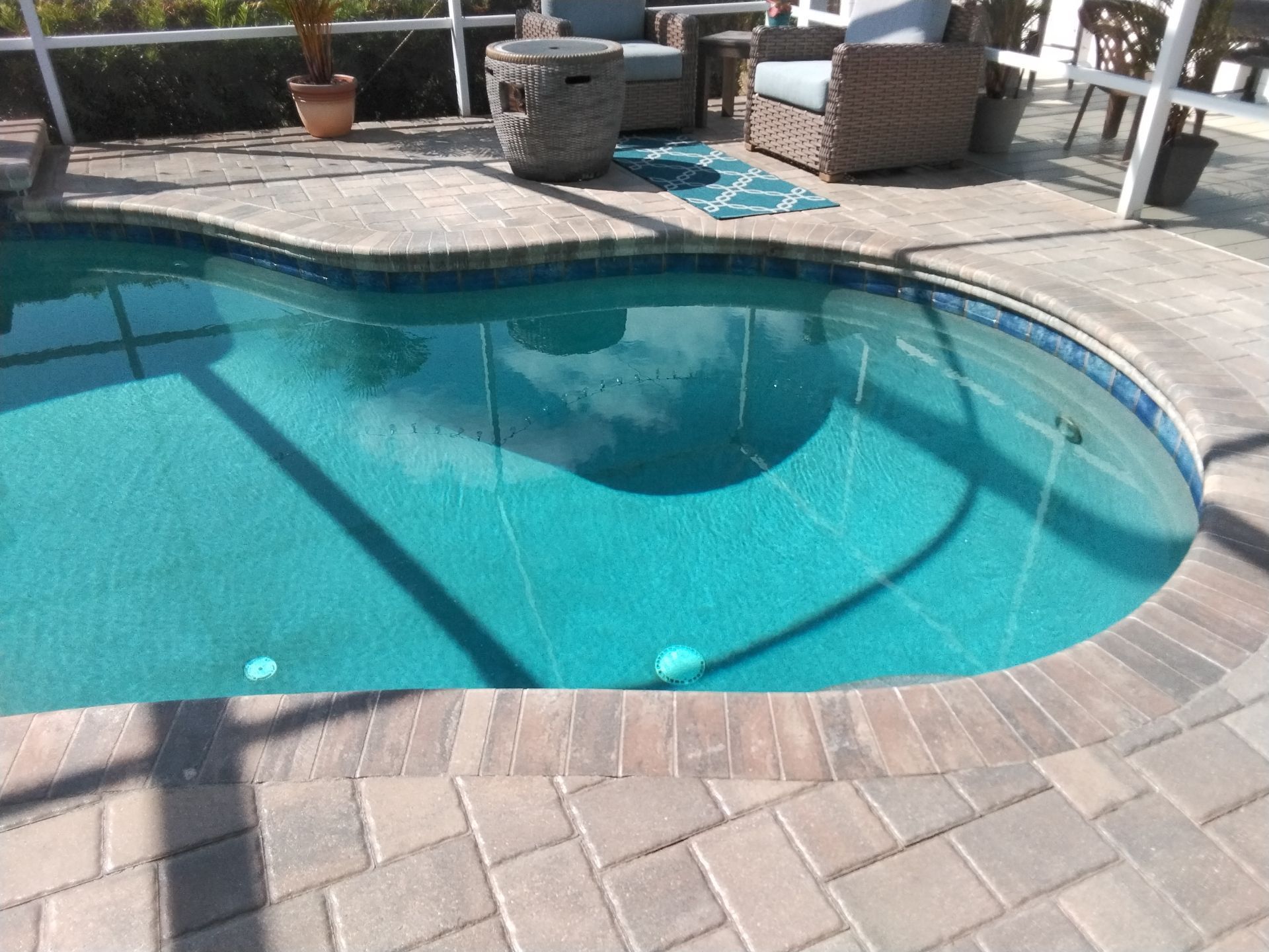 Backyard swimming pool with turquoise water, stone patio, and outdoor chairs in the sun.
