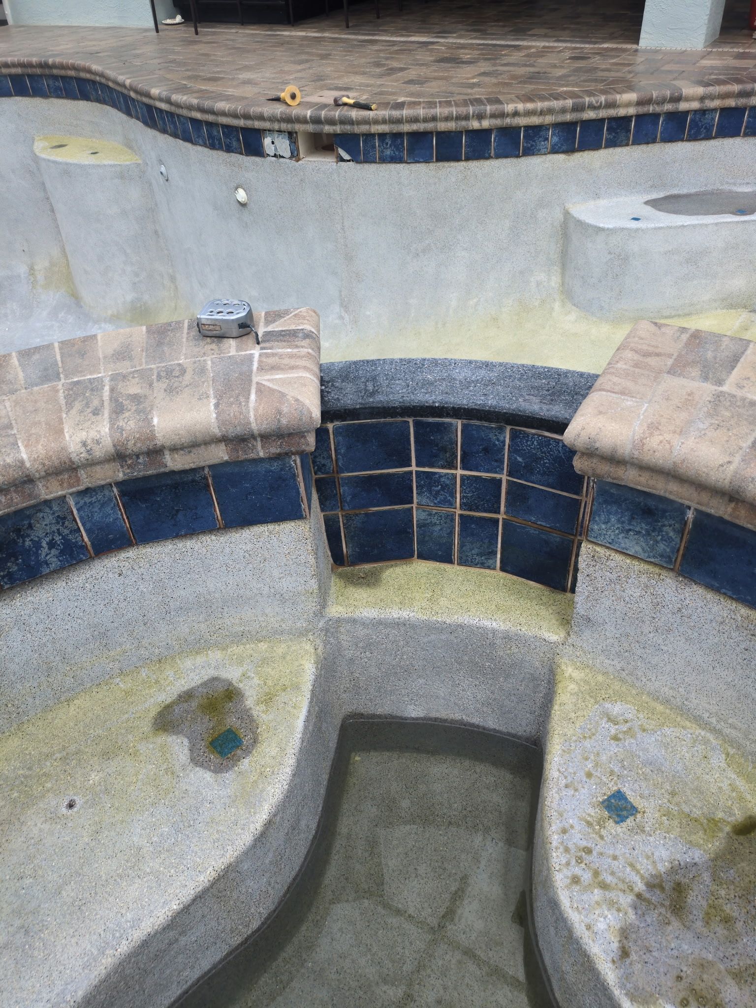 Empty tiled swimming pool with curved beige walls, dark blue tile band, and built-in benches.
