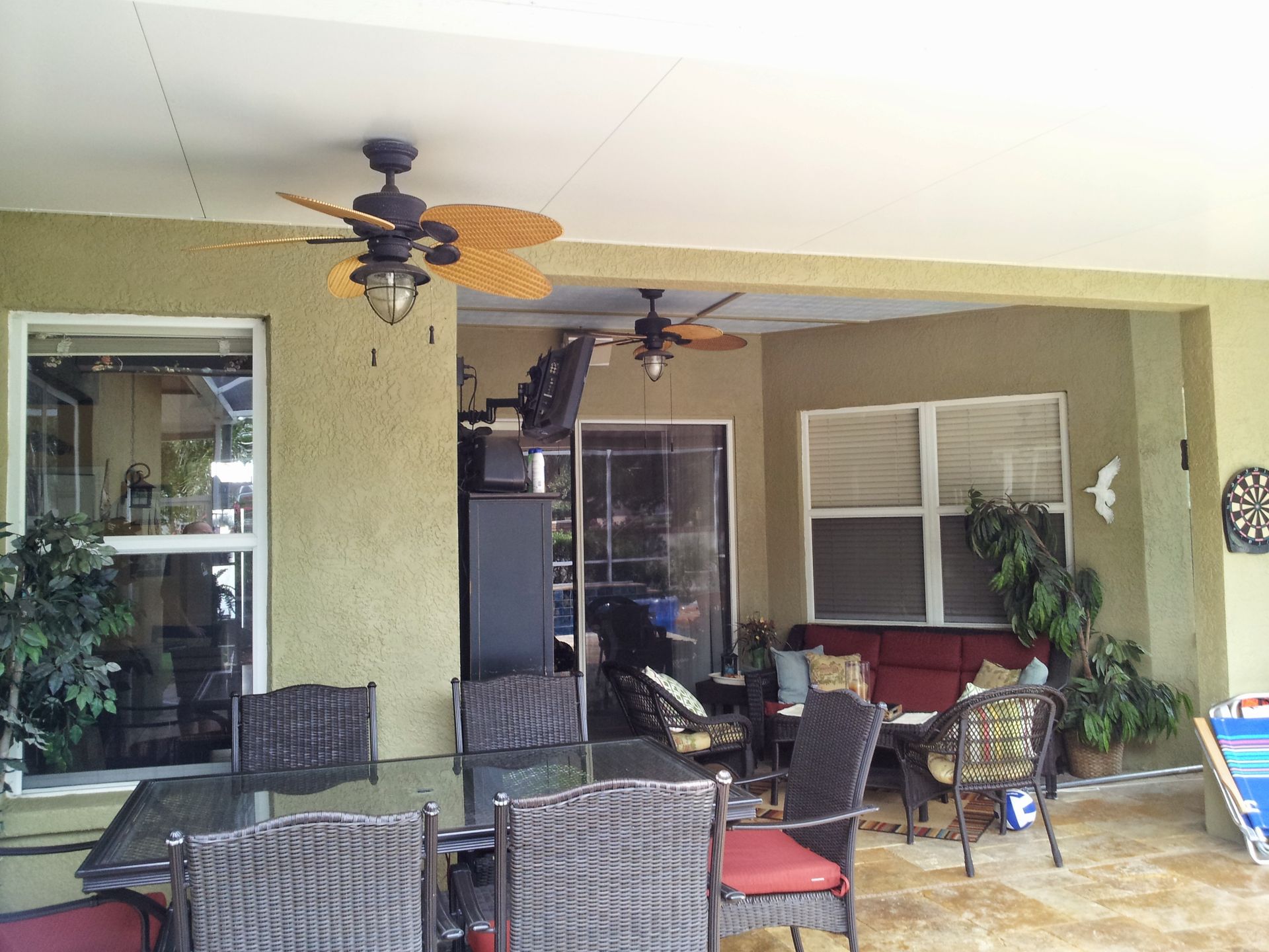Covered patio with wicker chairs, ceiling fans, plants, and a sliding glass door leading inside