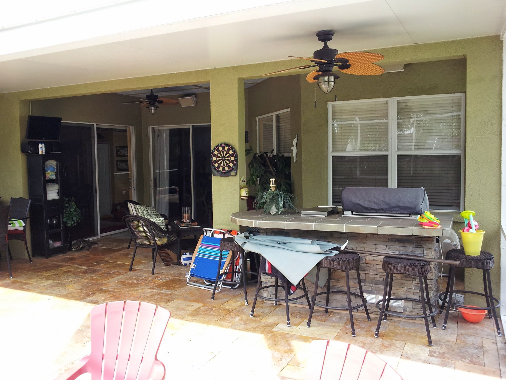 Covered patio with outdoor dining table, chairs, ceiling fans, and potted plants beside a house