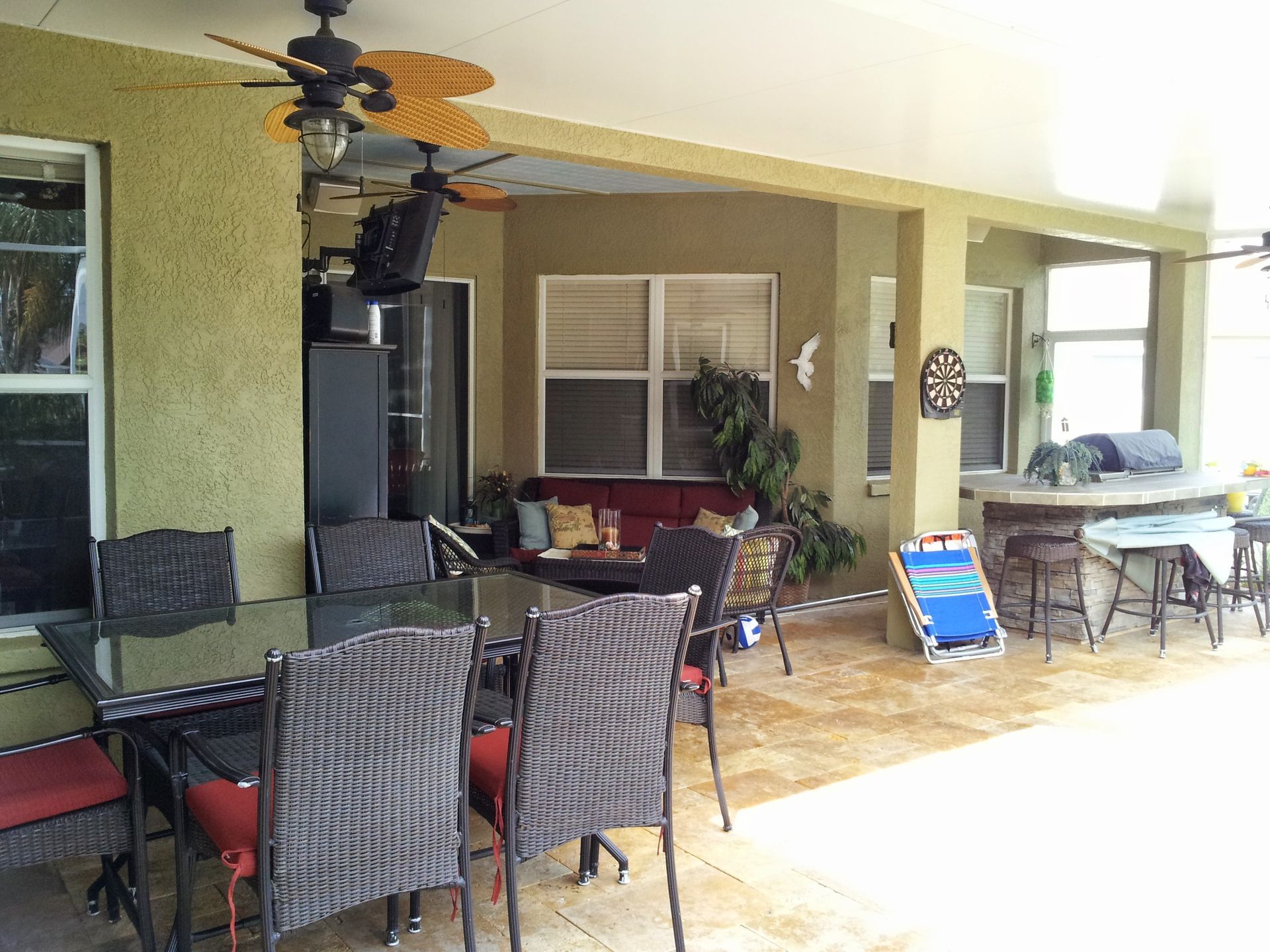 Covered patio with wicker dining chairs, tables, ceiling fans, and potted plants beside the house