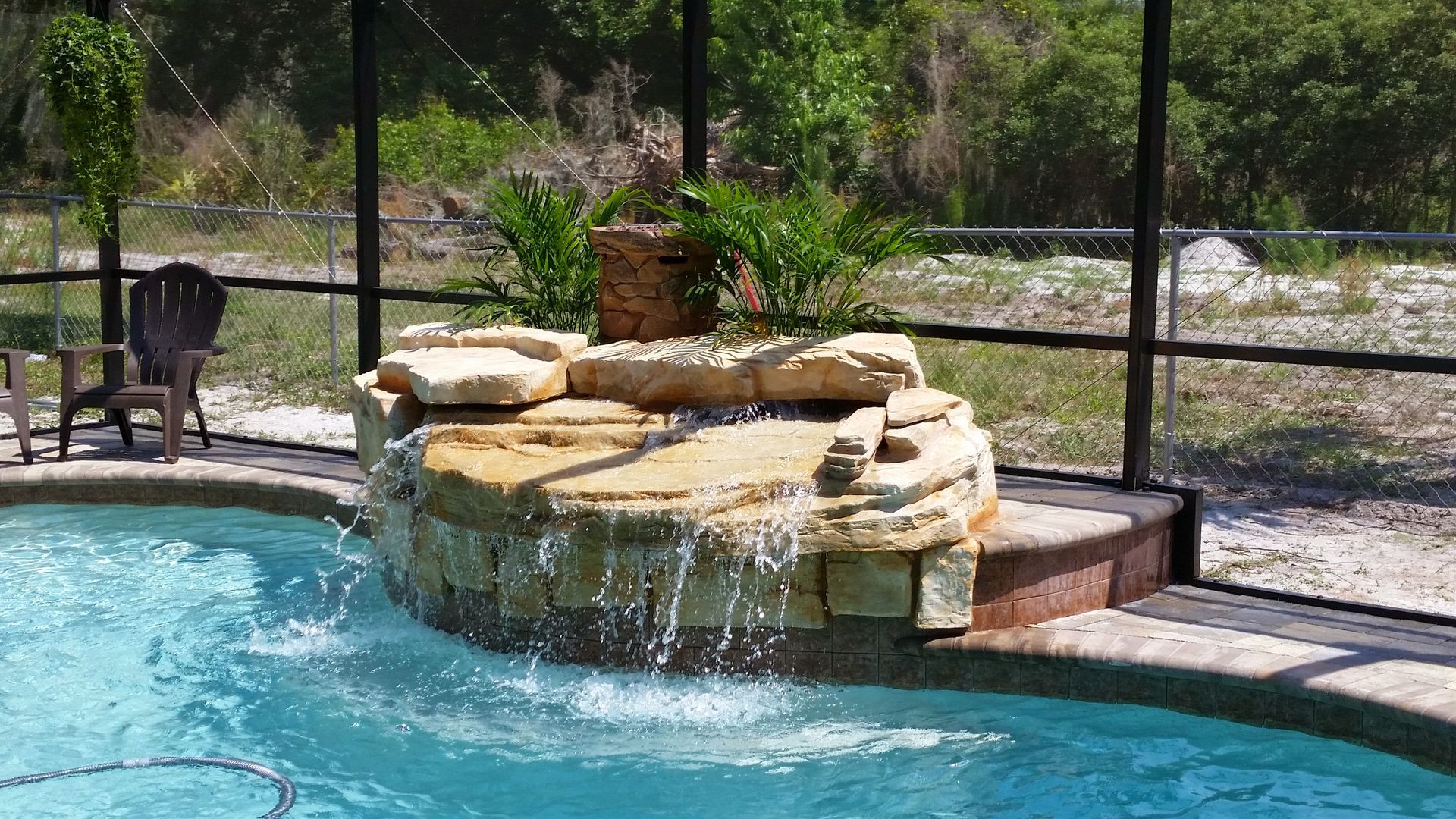 Backyard pool with a stone waterfall feature and a dog standing by the fence