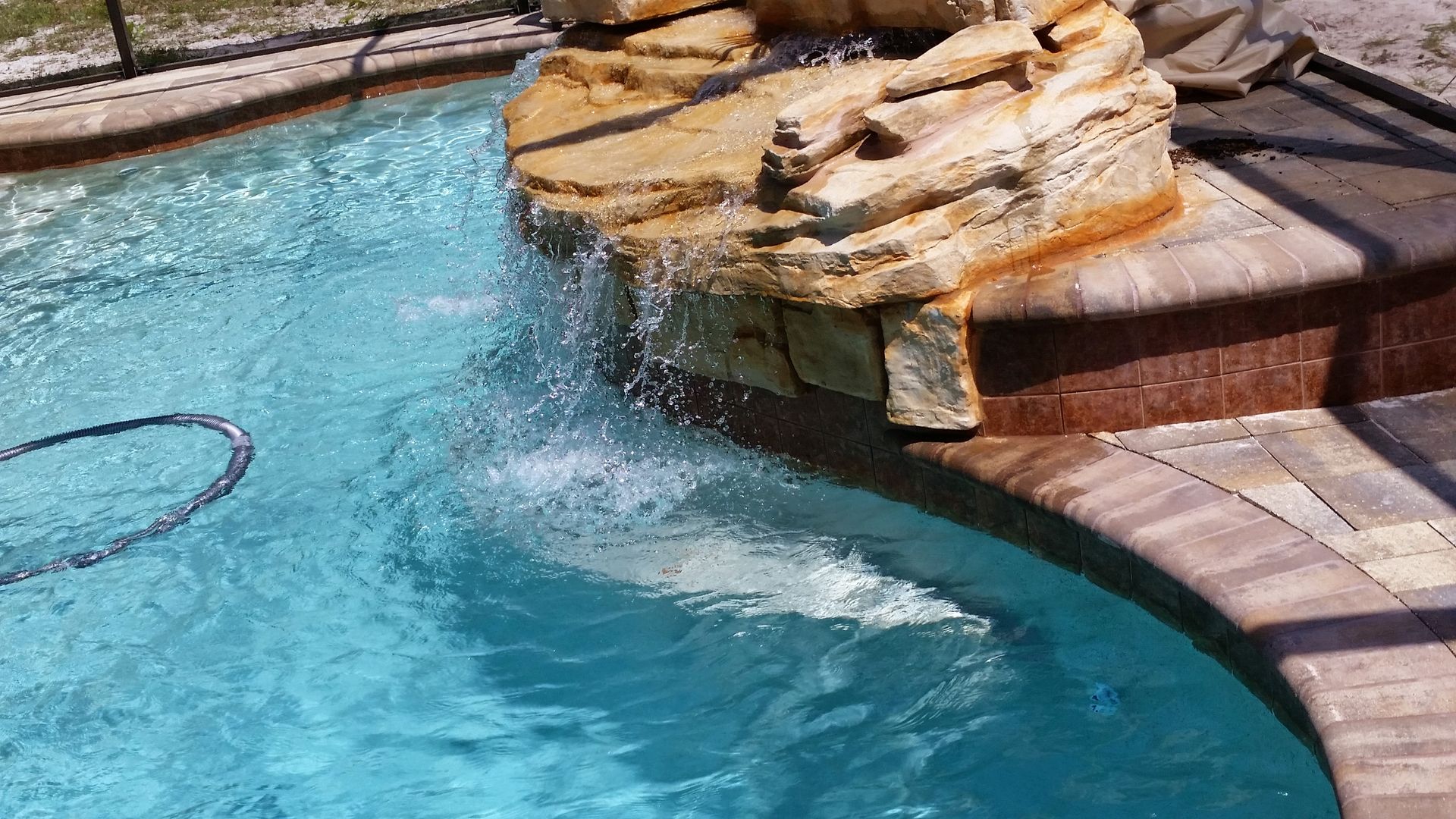 Curved backyard pool with blue water and a stone waterfall feature