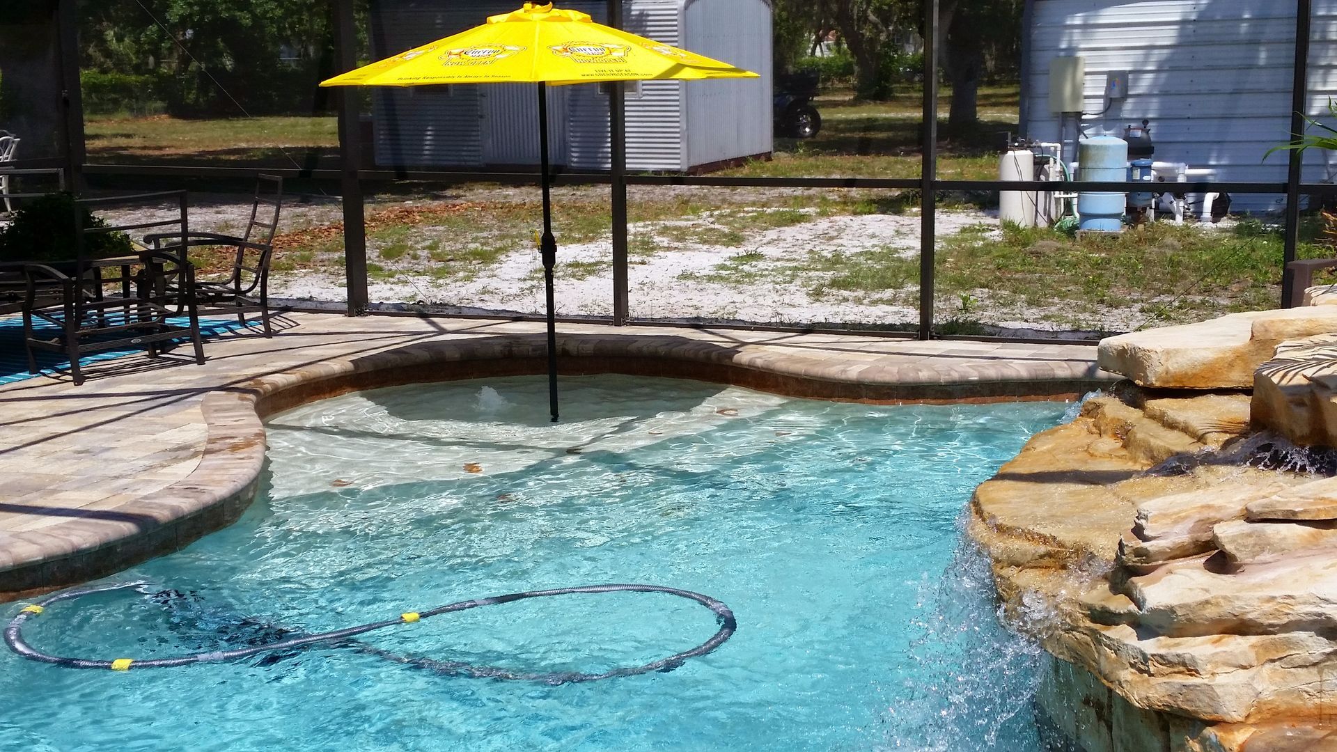 Backyard pool with bright yellow umbrella, stone edging, and clear blue water.