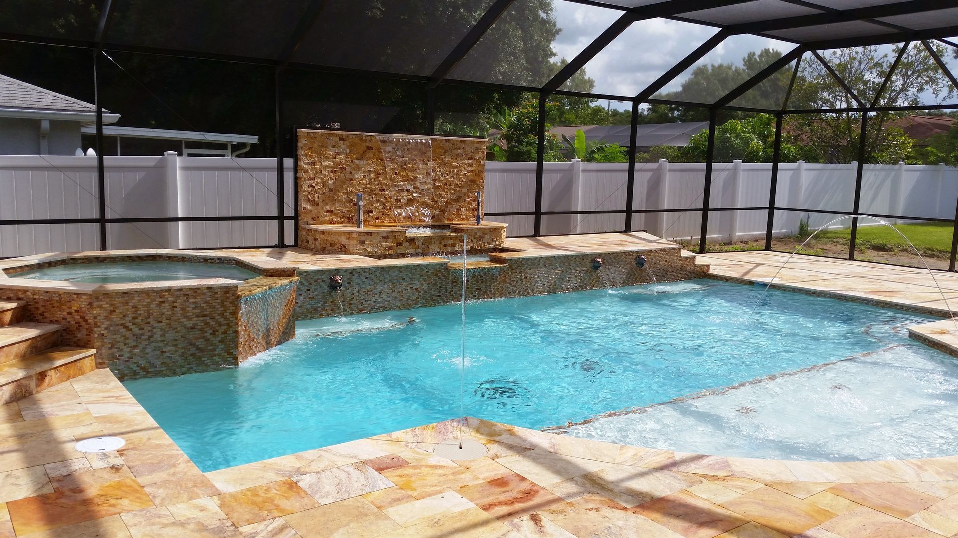 Indoor pool with turquoise water, stone waterfall feature, and screened enclosure under a dark roof.