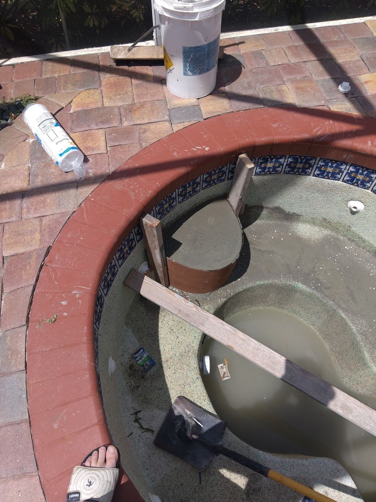 Open hole in brick paving with makeshift wooden crossbars and buckets nearby.
