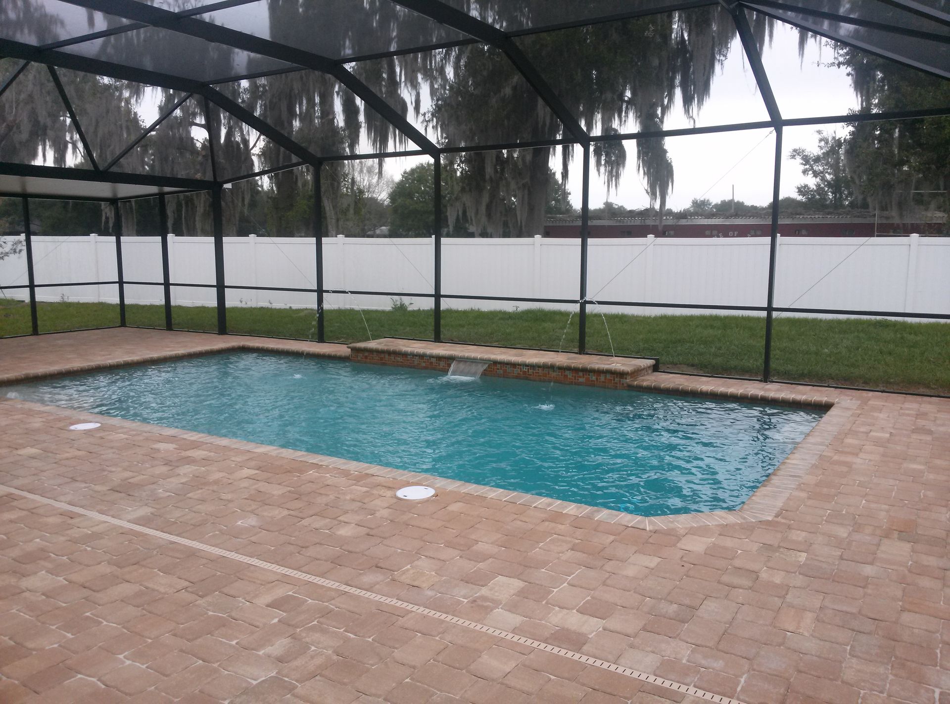 Rainy backyard patio with a screened-in swimming pool and brick pavers.