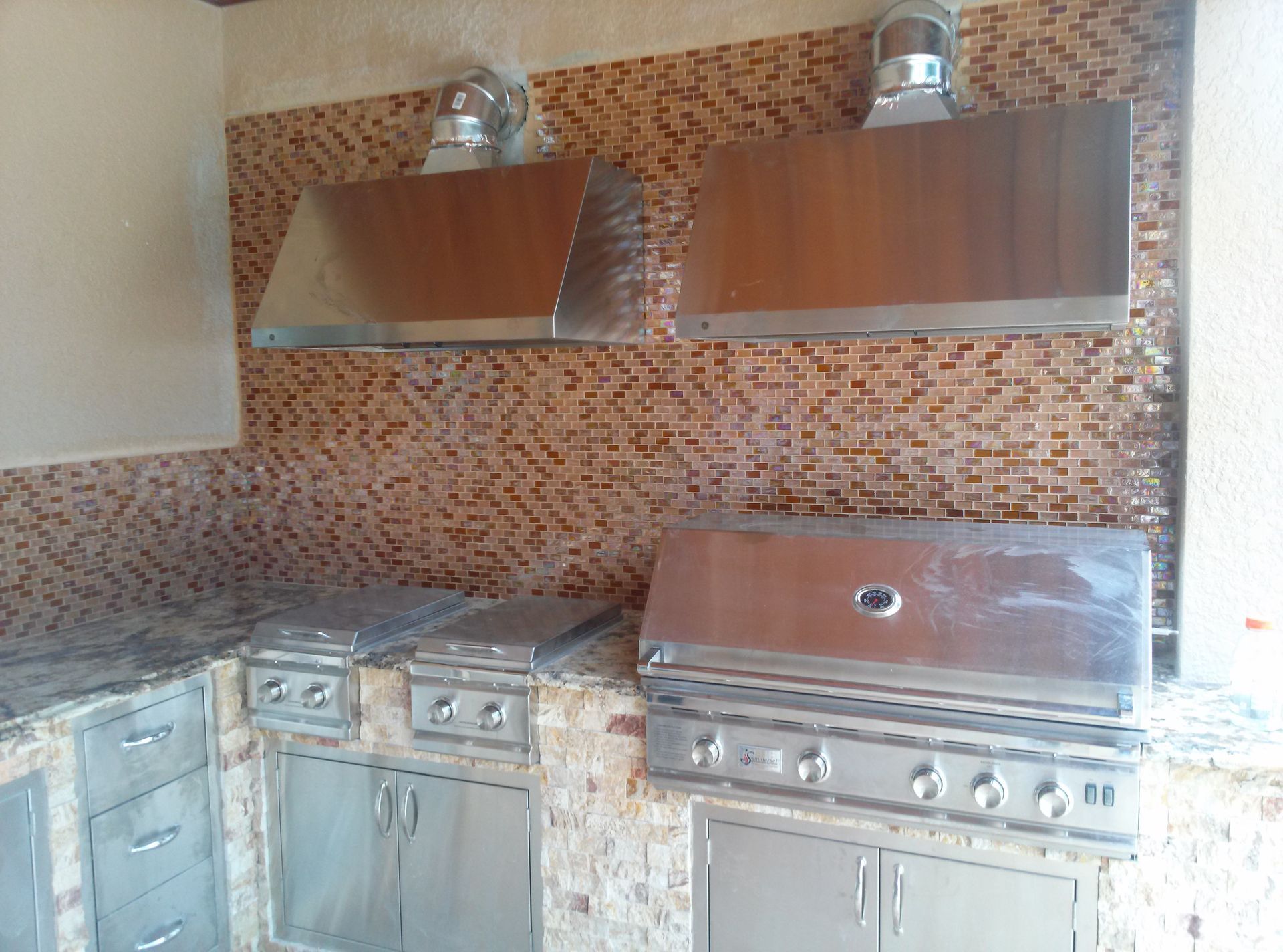 Modern kitchen with stainless-steel stove, two range hoods, and mosaic tile backsplash