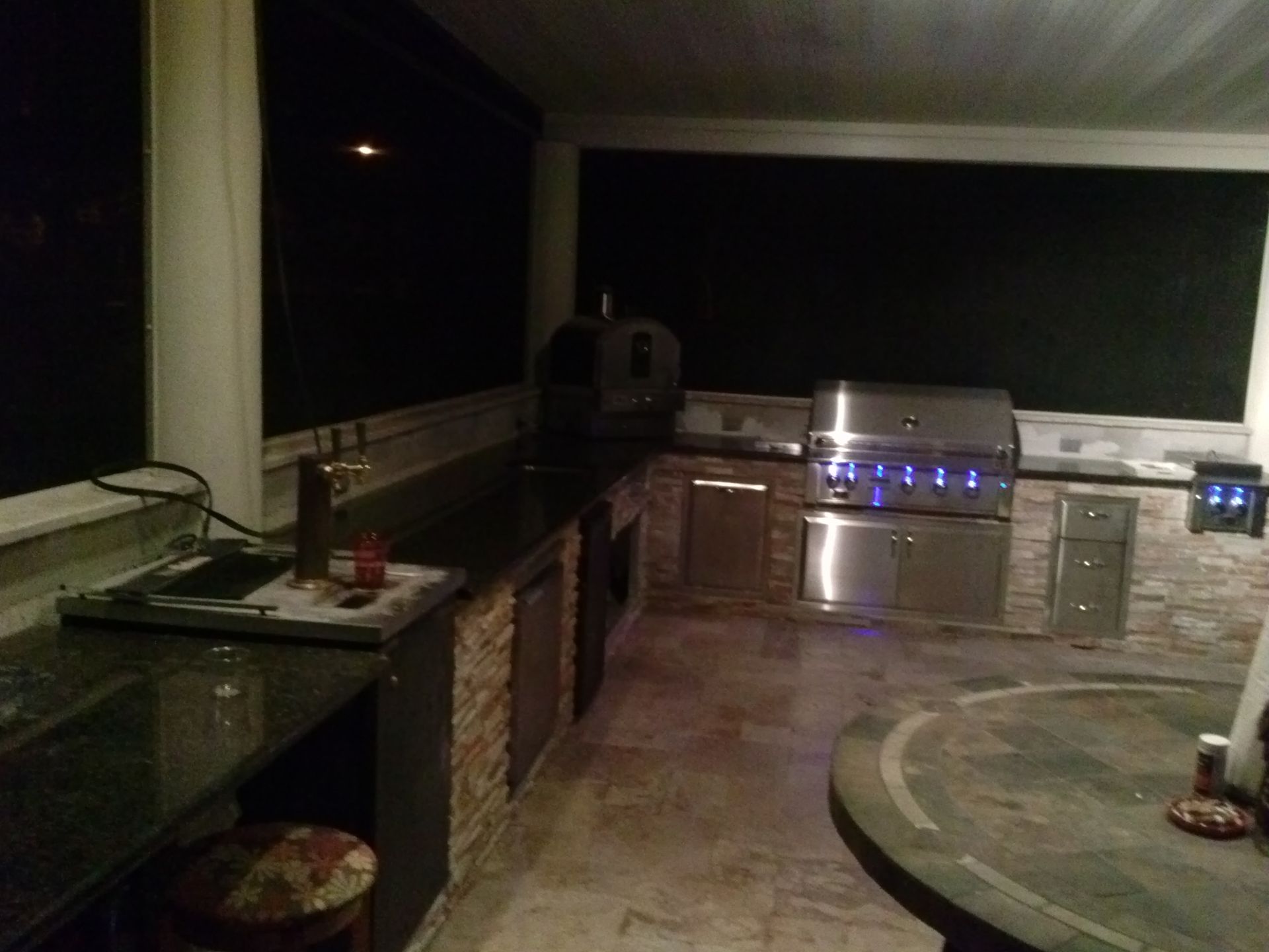 Outdoor kitchen patio at night with grill, countertops, cabinets, and curved stone seating area
