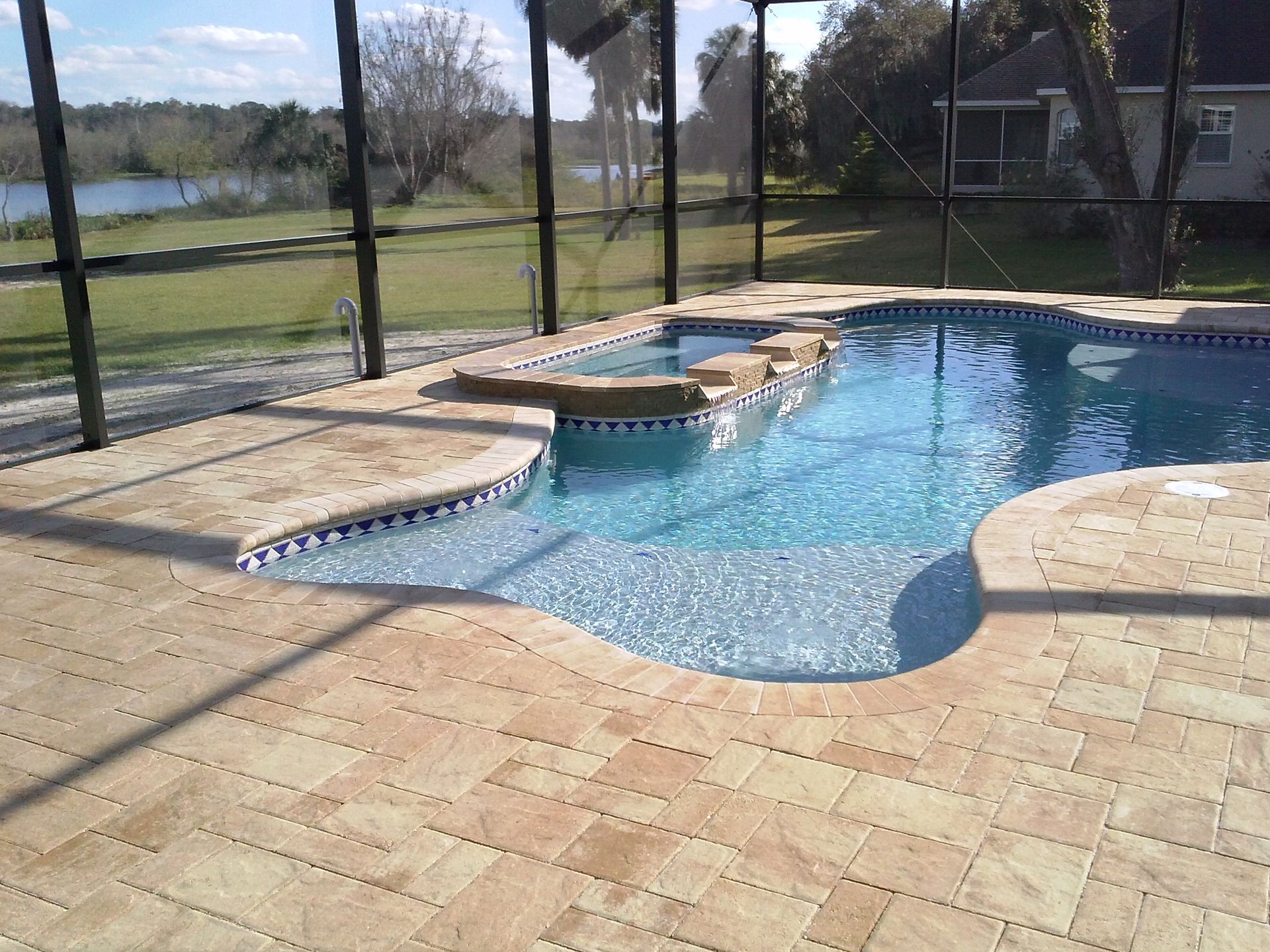 Backyard swimming pool with blue water, stone deck, and screened enclosure