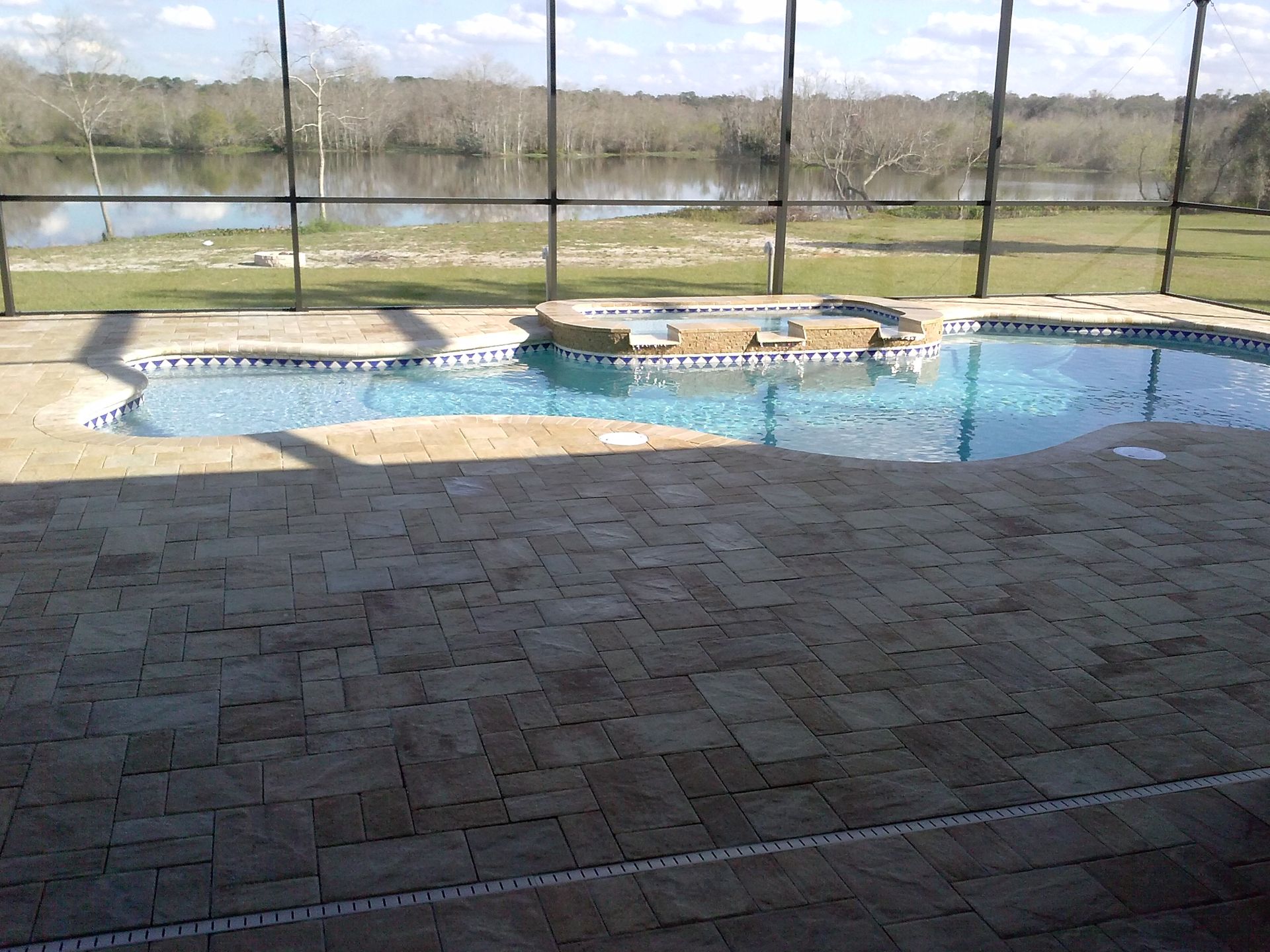 Outdoor pool with stone deck and screened enclosure overlooking a grassy landscape