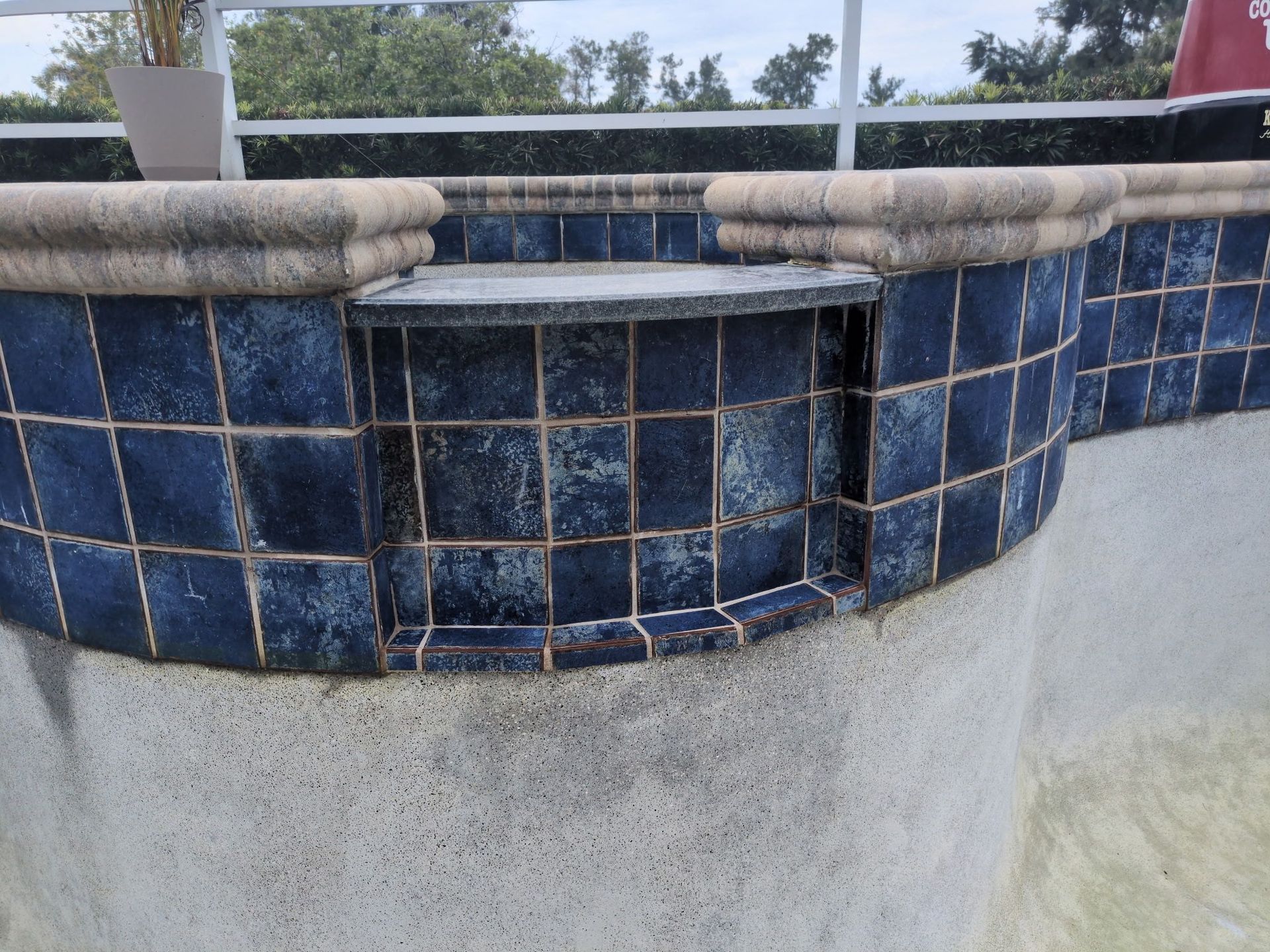 Blue-tiled pool spa with a raised ledge and white stone coping outdoors.