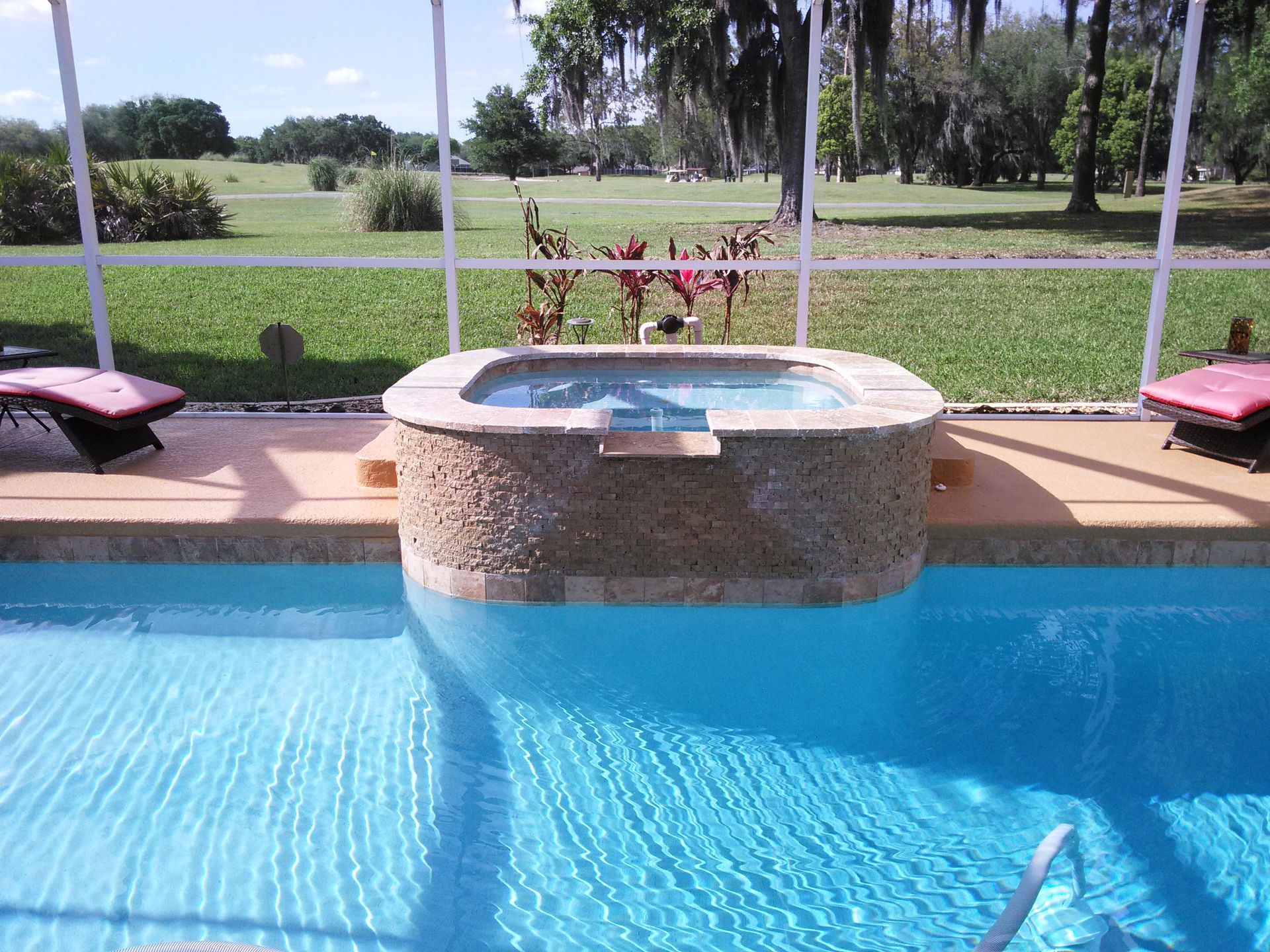 Backyard pool with a raised circular hot tub, lounge chairs, and a view of a green lawn beyond the fence.