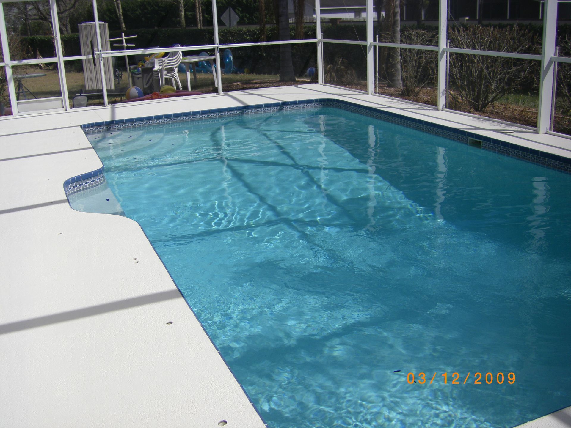 Swimming pool with clear blue water beside a white deck and screened enclosure