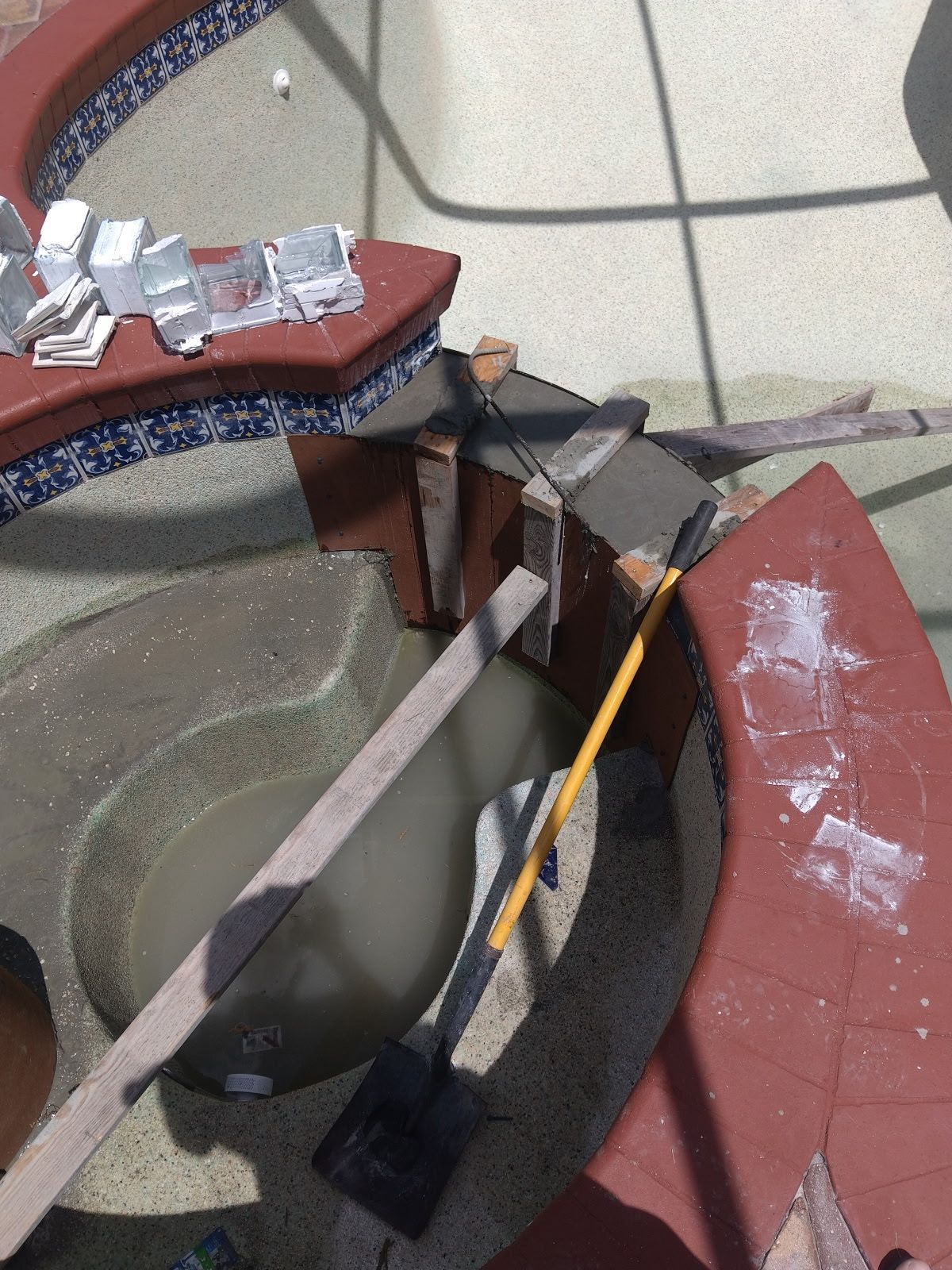Broken outdoor patio table with scattered debris, a broom, and a damaged red chair on a tiled floor.