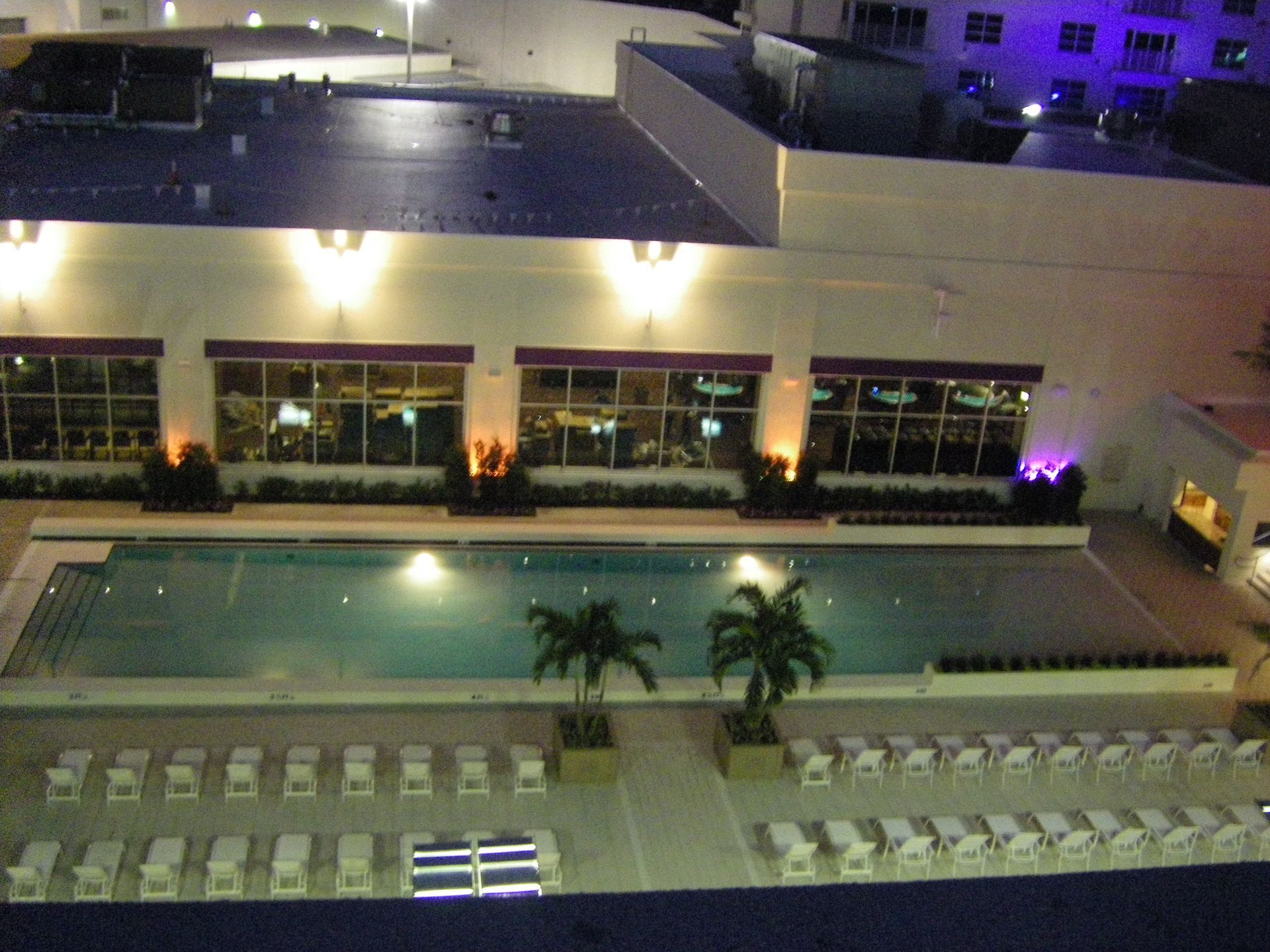 Nighttime view of a hotel pool courtyard with lounge chairs and purple-lit building windows
