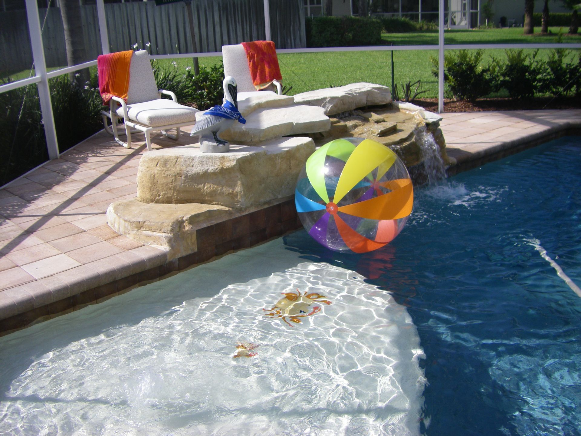 Colorful beach ball floating in a backyard pool beside stone steps and lounge chairs