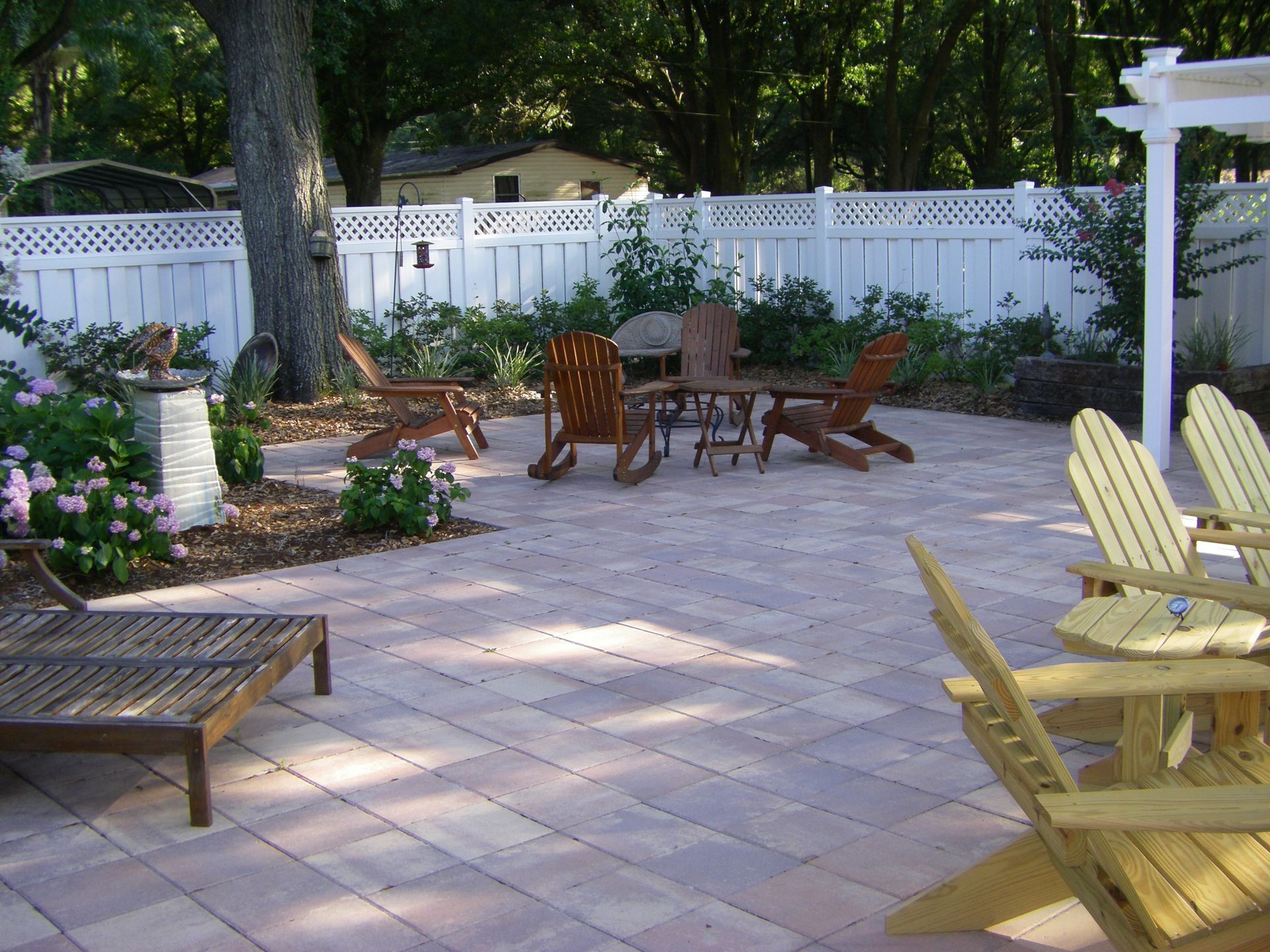Patio with wooden chairs and tables on a stone patio beside white fencing and garden flowers