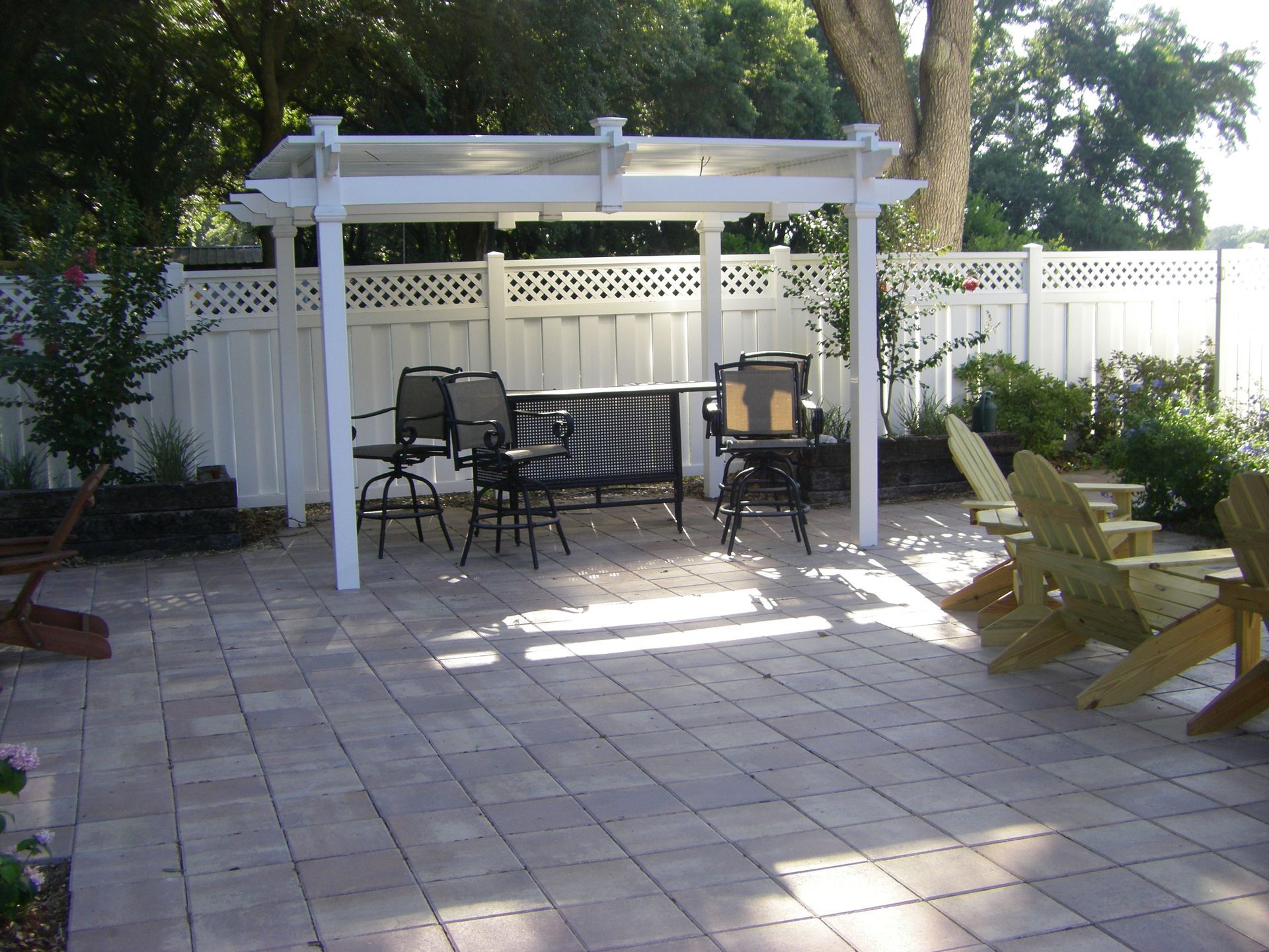 Patio with white pergola, table and chairs, wooden lounge chairs, and a fence in the background