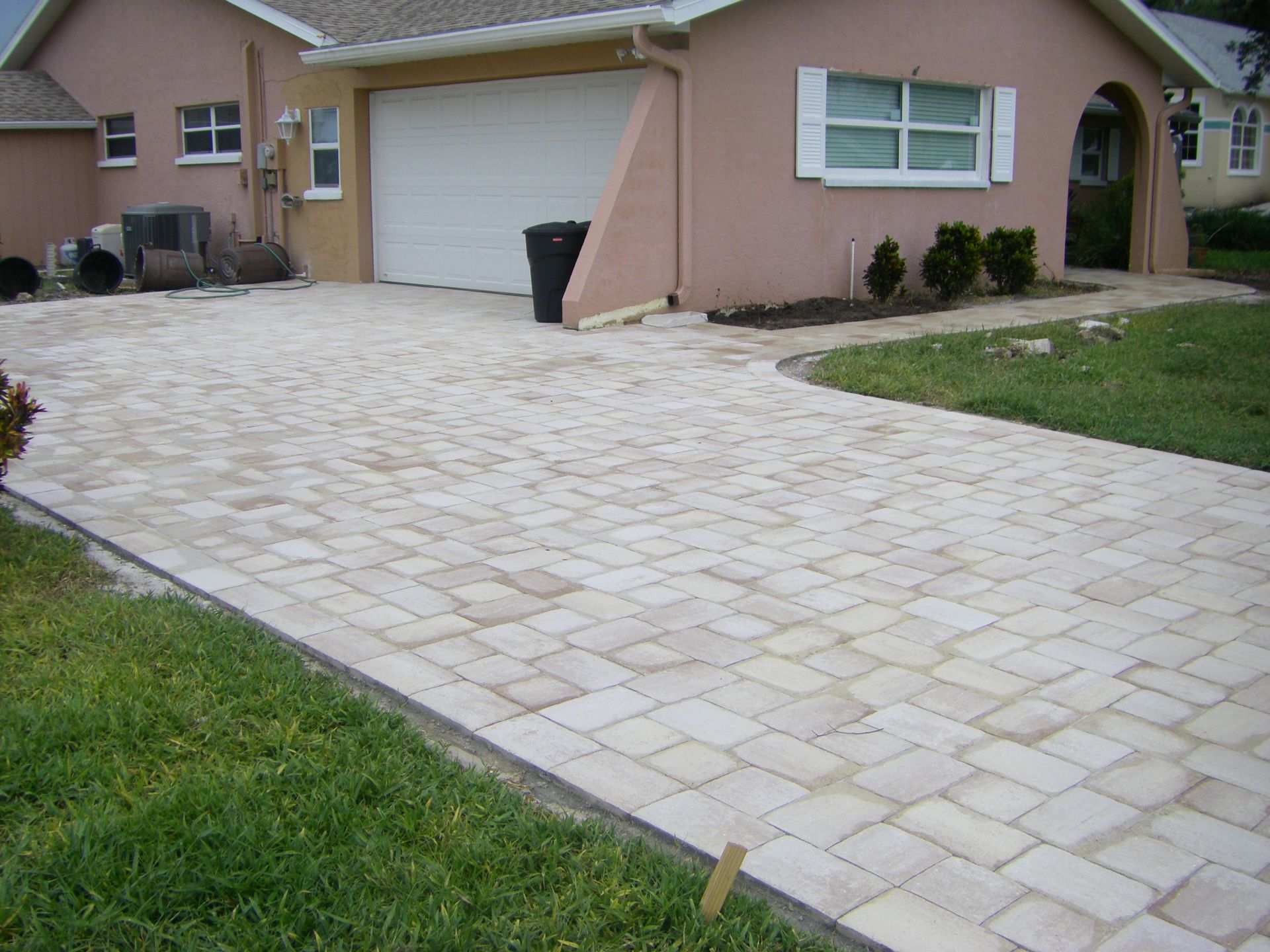Paved driveway leading to a garage and front door of a beige house, with grass along the edge.