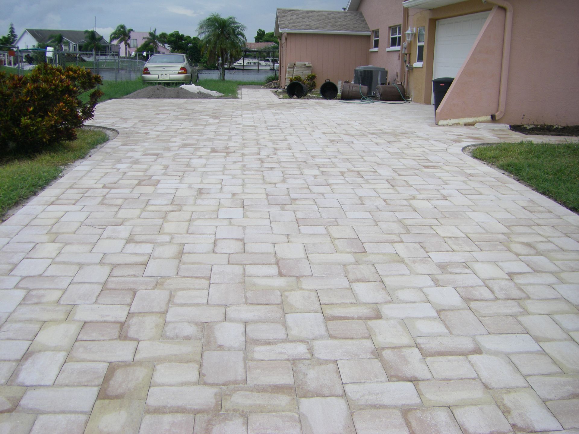 Paved stone driveway leading to a house, with lawns and a quiet residential street in the background
