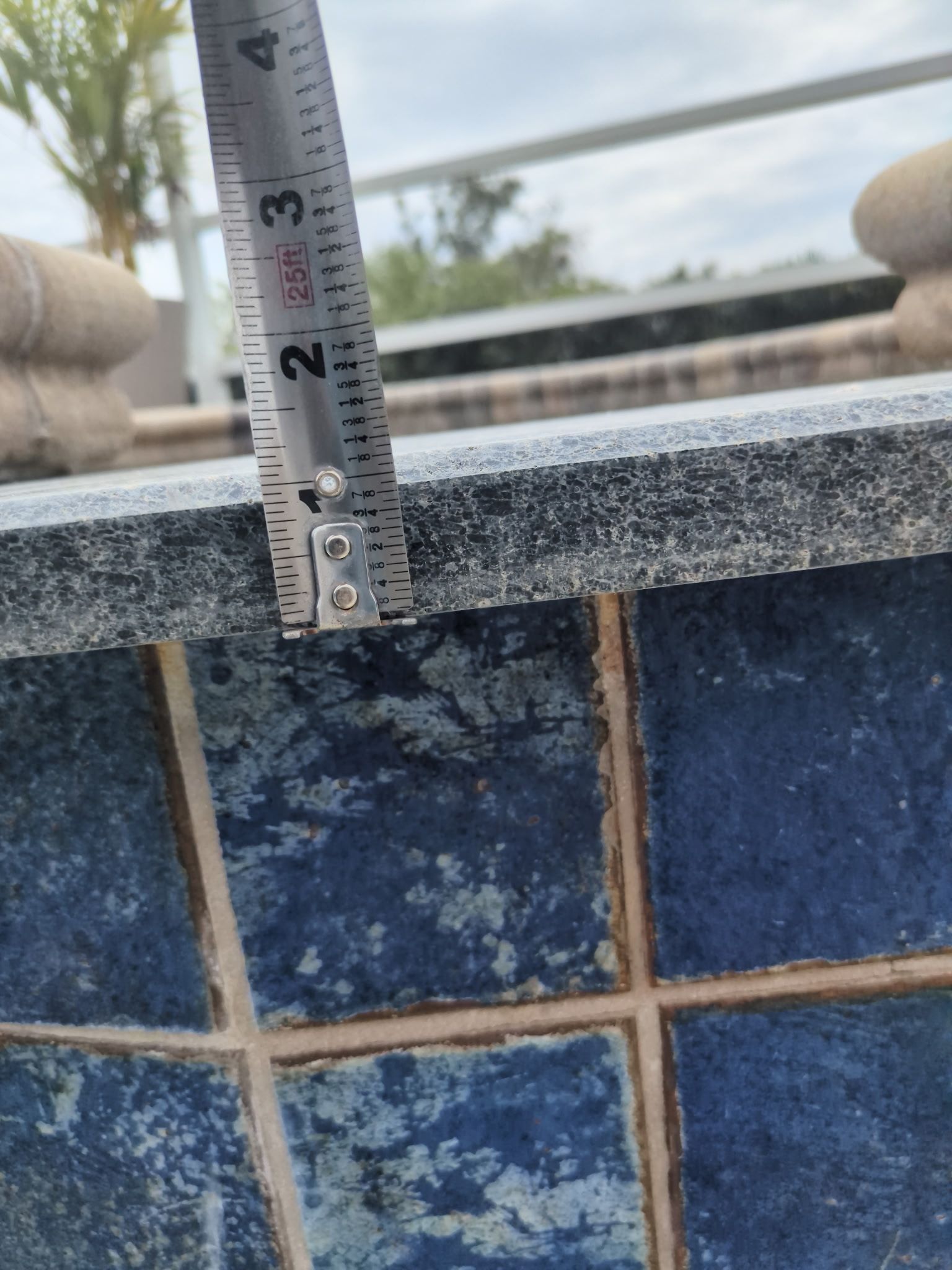 Tape measure on a chipped blue-tiled pool edge, showing the pool coping height.