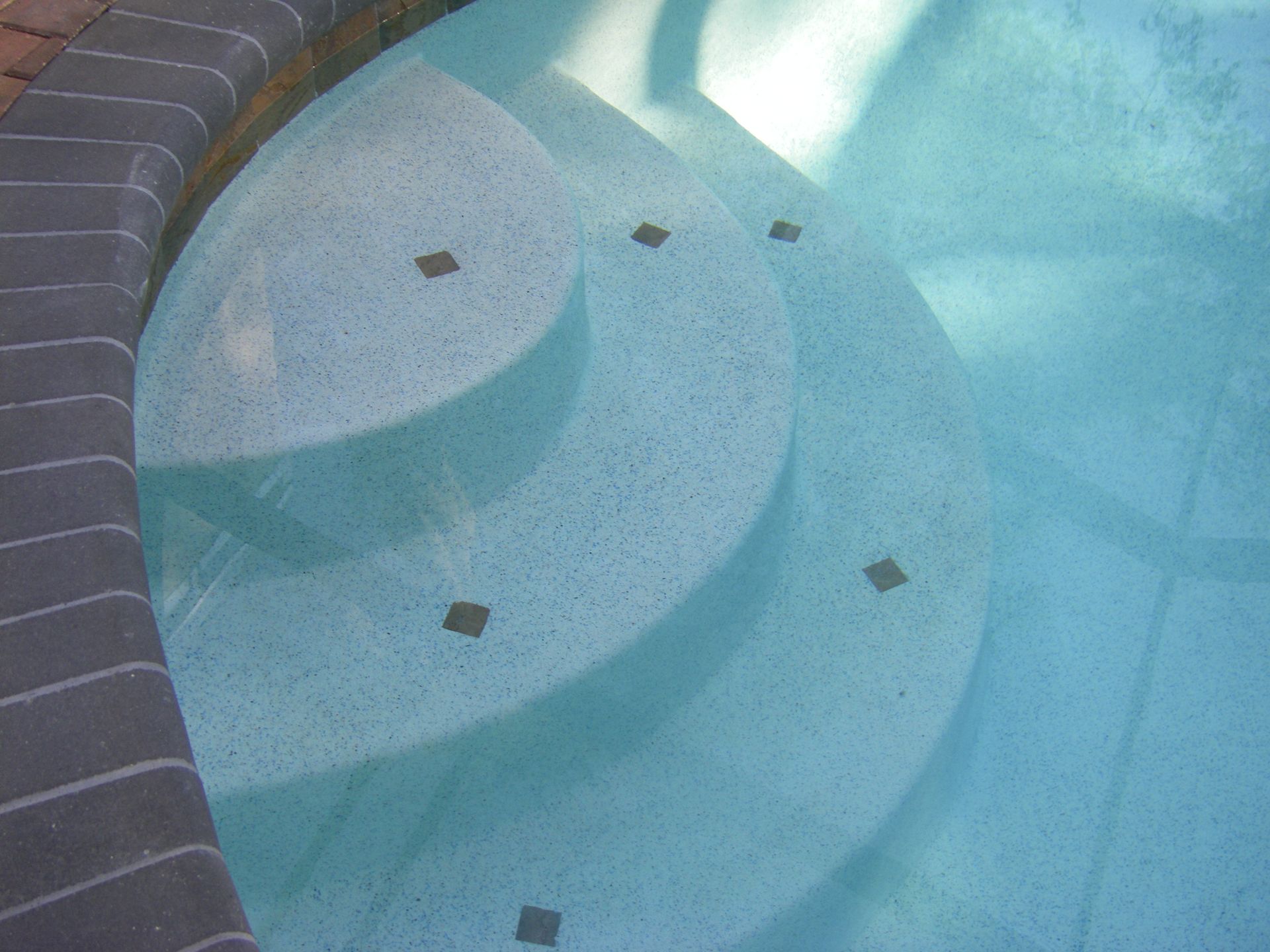 Curved mosaic-tiled pool steps descending into clear blue water