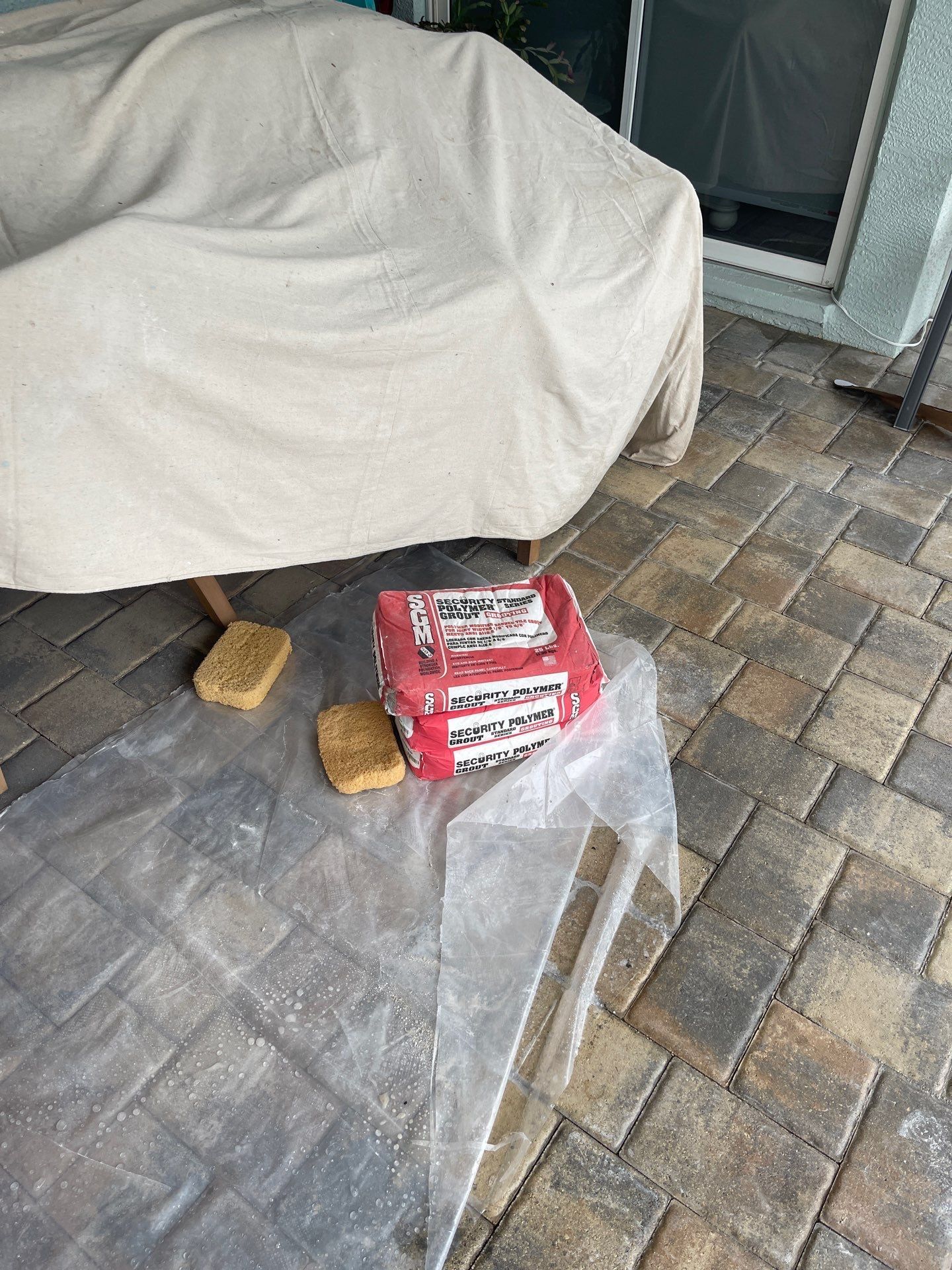 Covered patio chair with red package on brick pavers, beside a clear acrylic panel and two small brush heads.