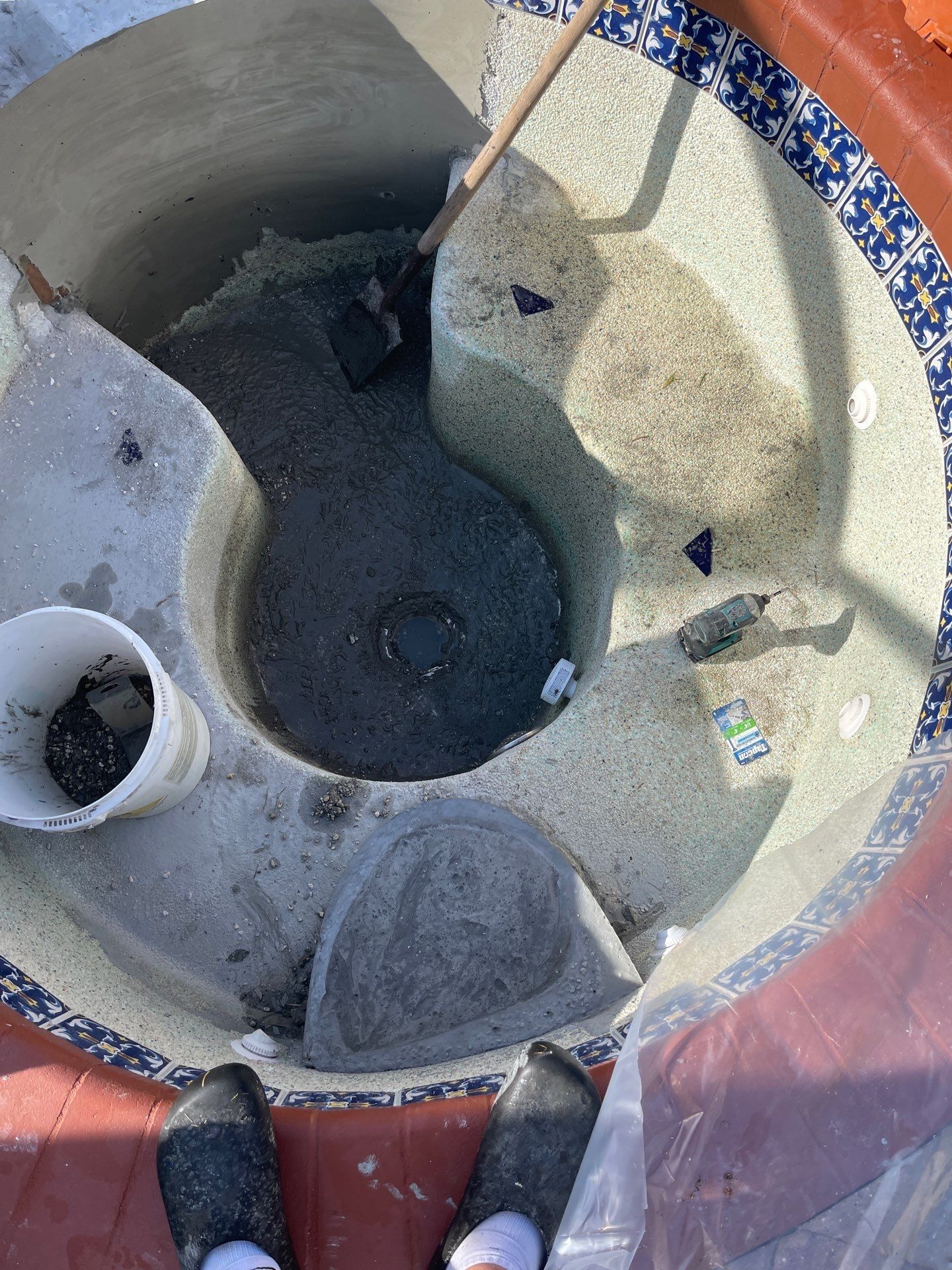 Overhead view of a gray bucket with water and ice on a tiled floor, with a broom and shoes visible nearby.