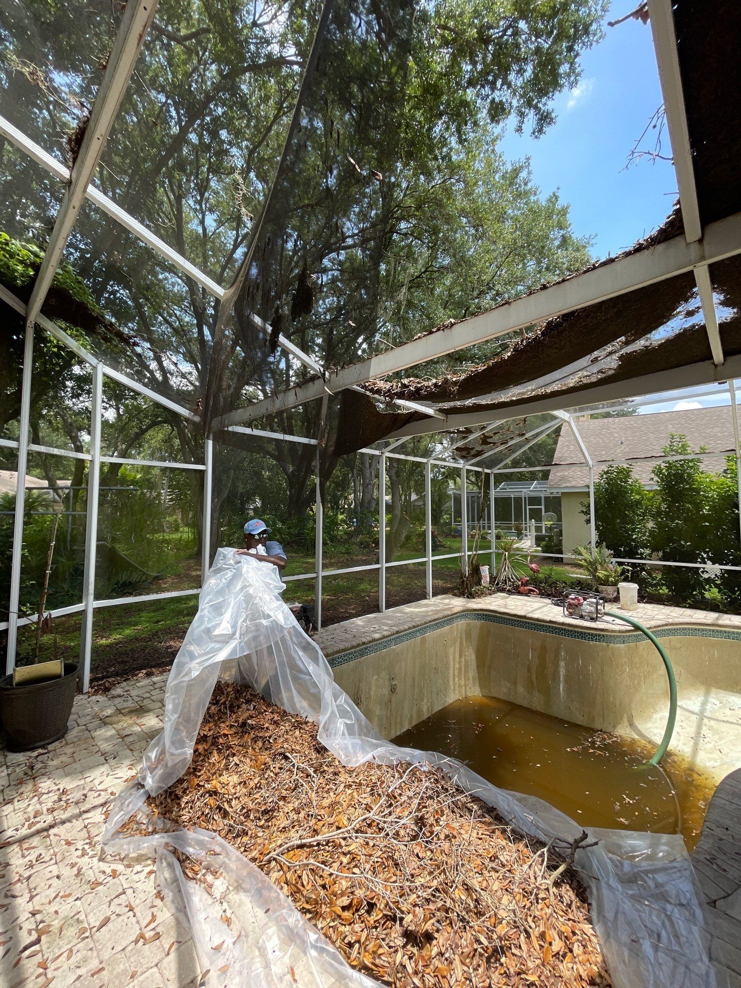 Person in protective coveralls working beside a drained pond with leaves and netted enclosure outdoors.