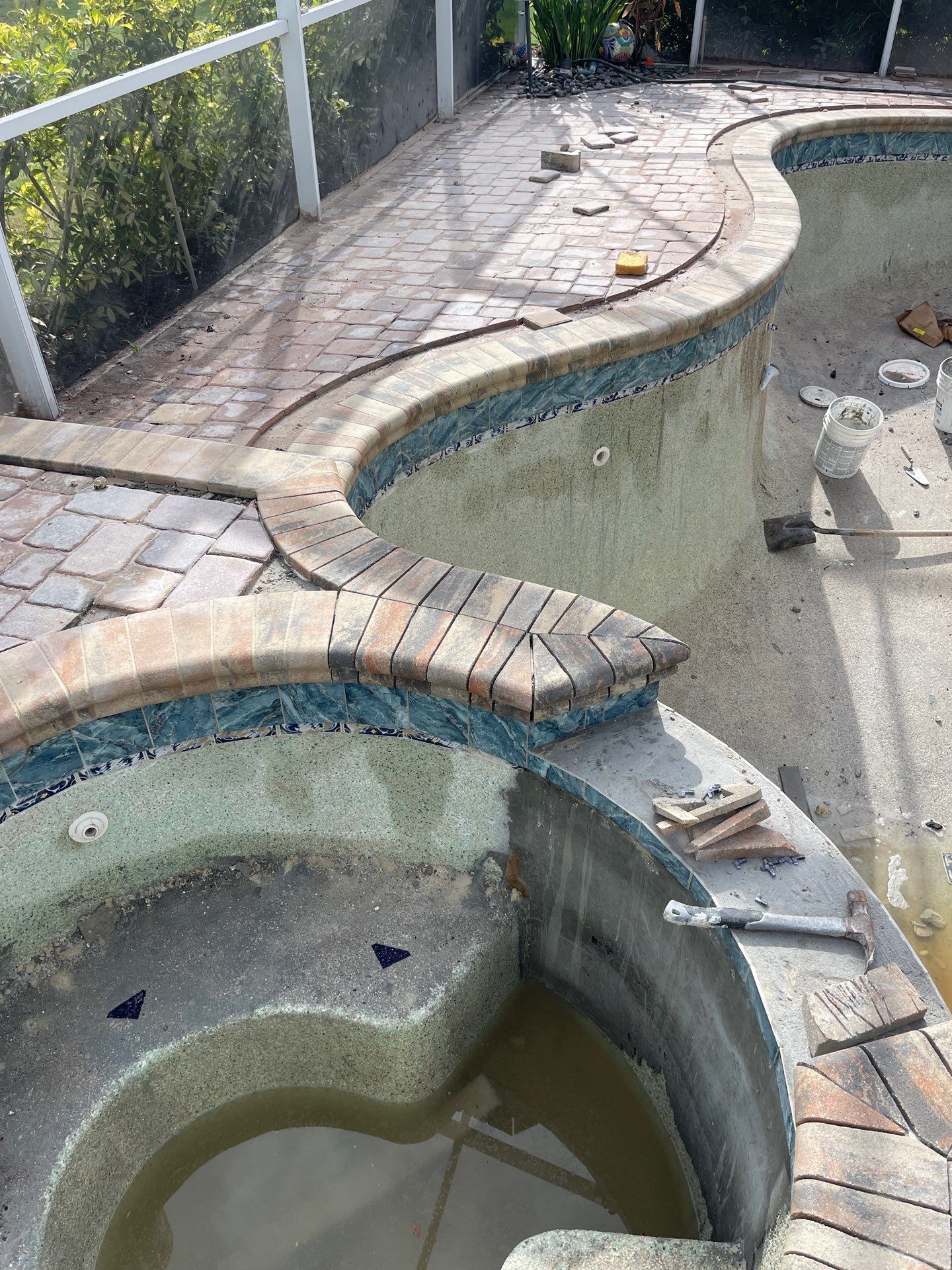 Empty, neglected swimming pools with cracked tile and murky water outdoors.
