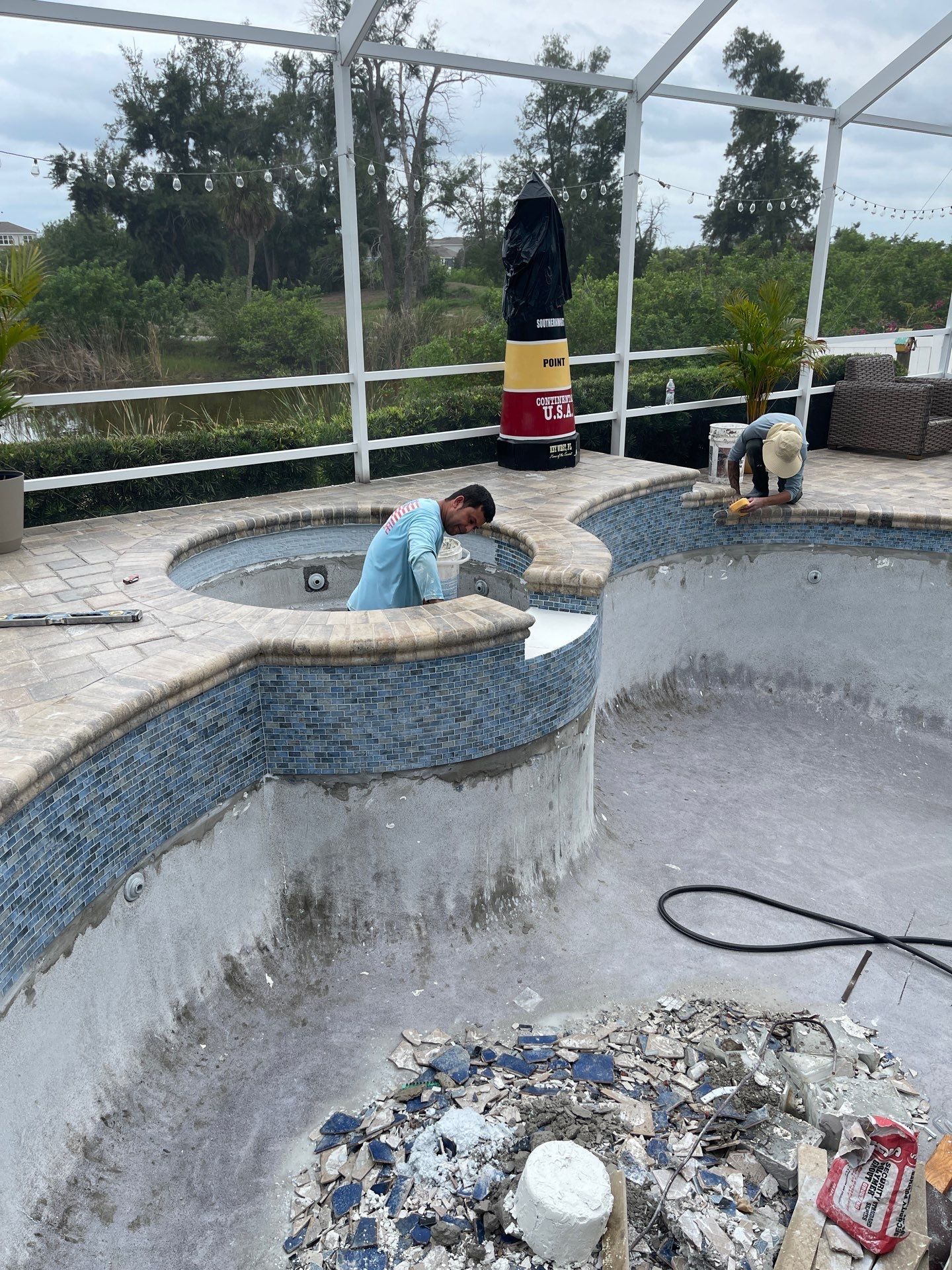 Workers cleaning a drained pool, with one inside and another at the edge near a black punching bag on deck.