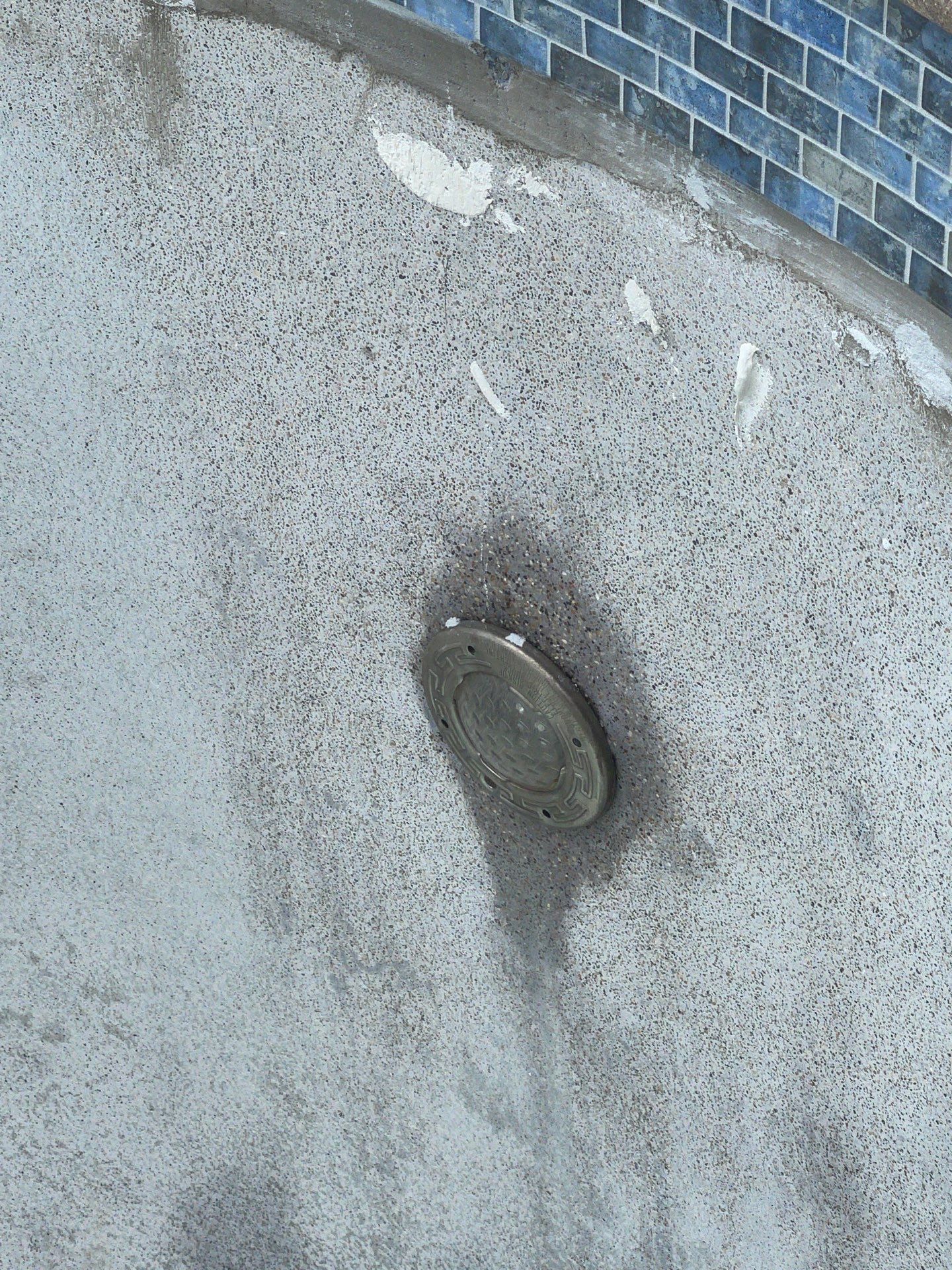Close-up of a metal screw or plug embedded in a gray concrete surface with dark water stains.
