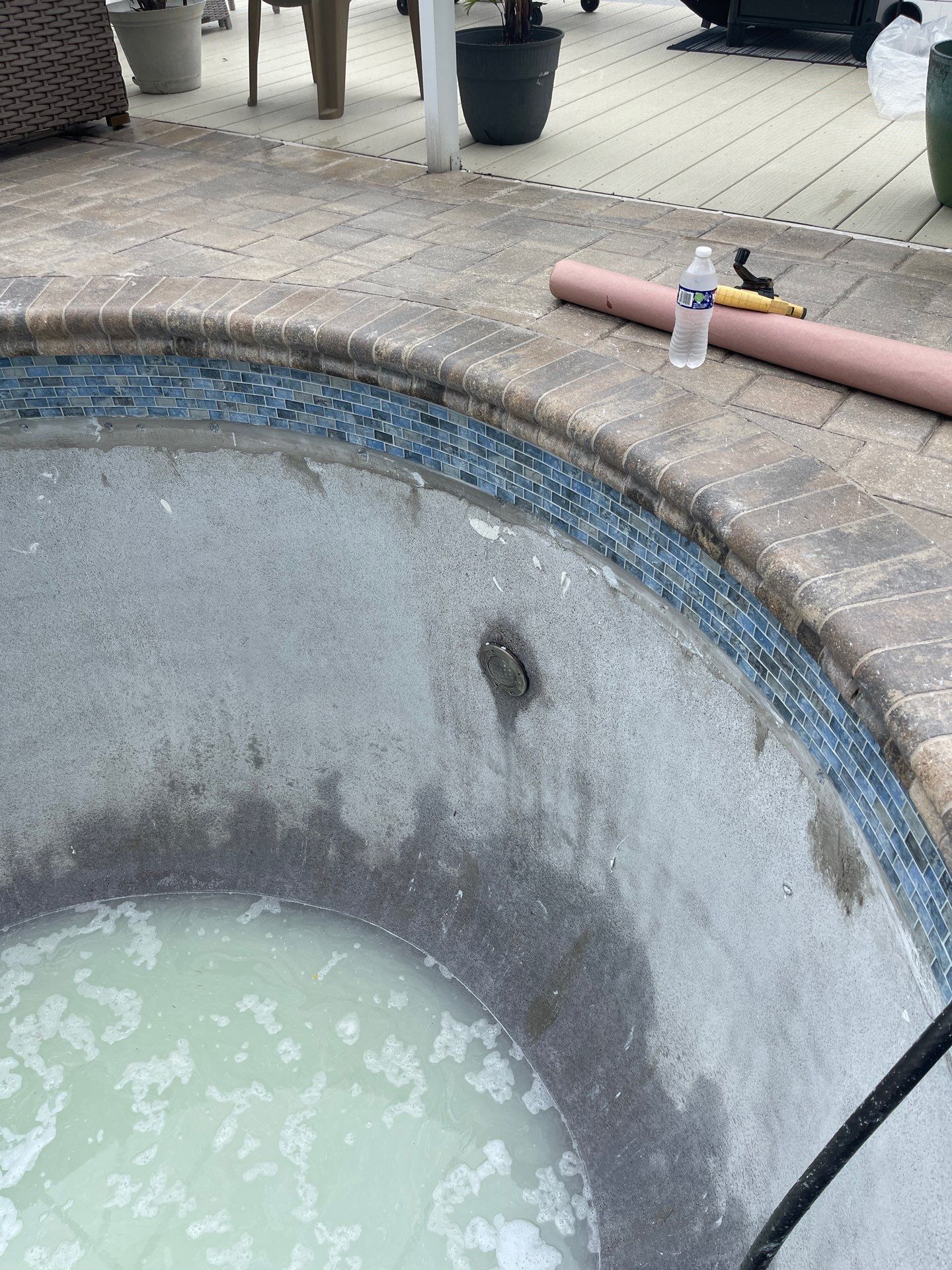 Empty pool with cloudy water, curved stone edge, and a hose on the deck above.