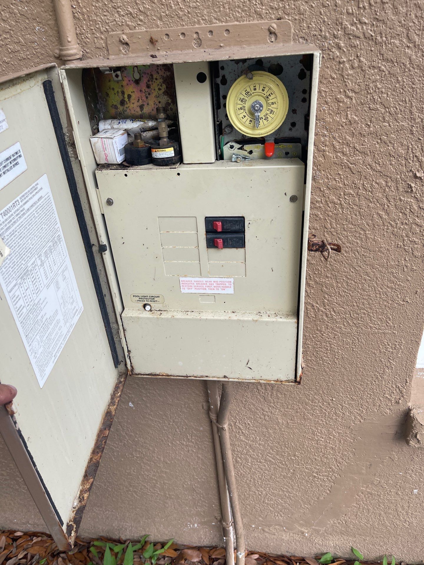 Open electrical breaker panel on a stucco wall, showing breakers and wiring.