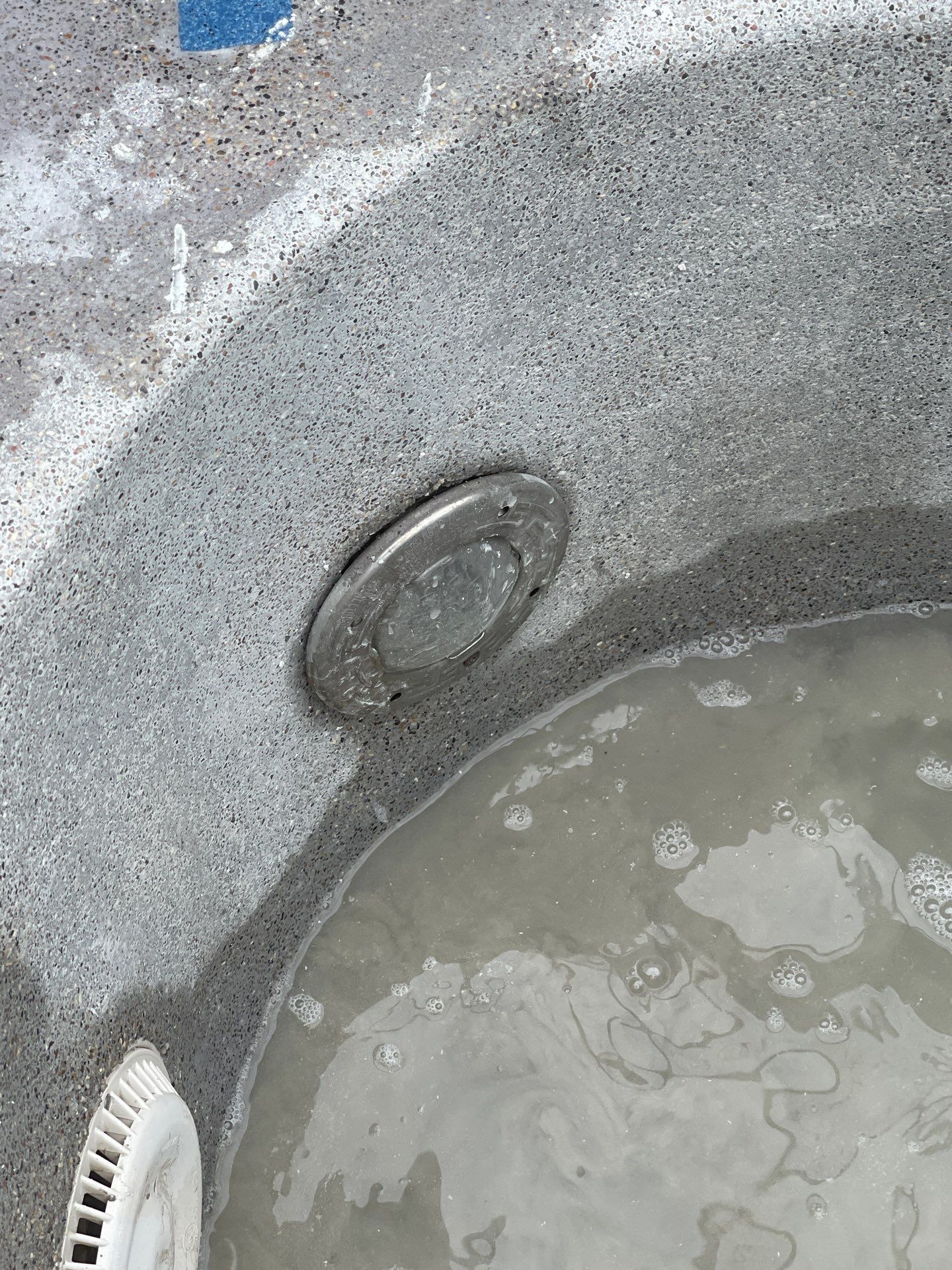 Dirty bathtub drain with standing soapy water and a scrub brush at the edge.
