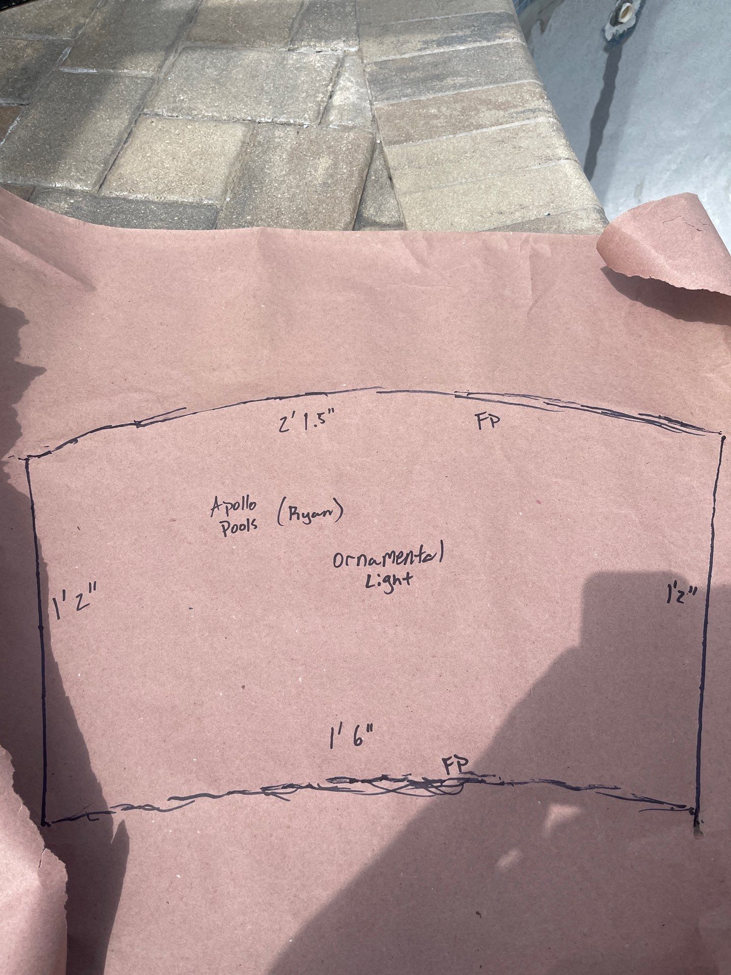 Hand-drawn pattern on pink paper with measurements, held outdoors on a paved surface.