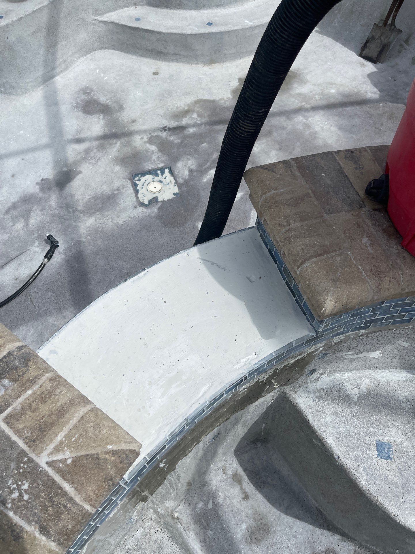 Poolside patio with white and brown tile, a black hose, and a red container edge.