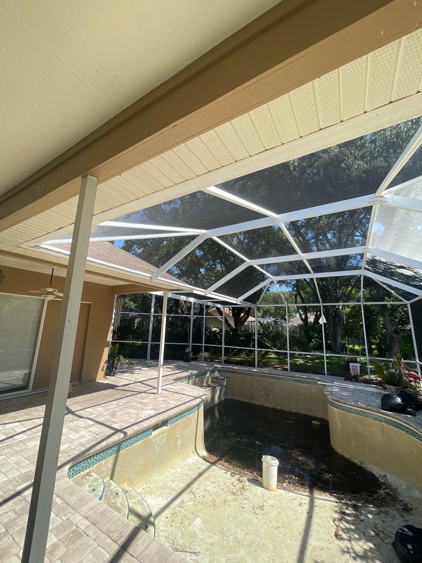 Screened patio with a tiled pool or spa, beige walls, and sunlight filtering through white beams.