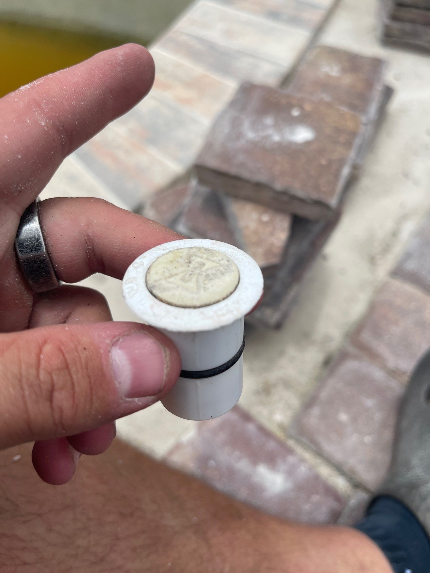 Hand holding a small white and black cylinder with a coin on top, outdoors on a paved surface.