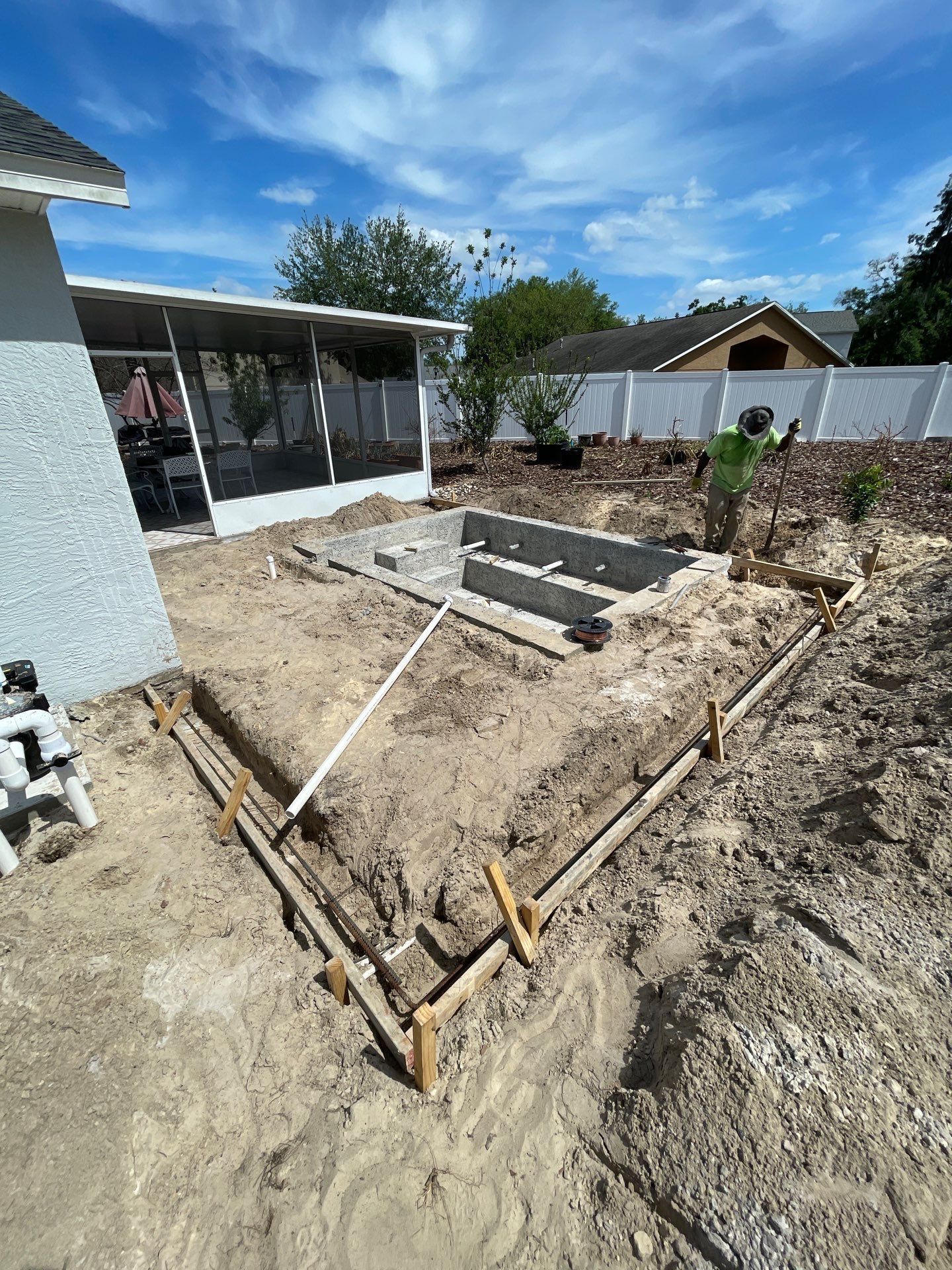 Backyard construction site with wooden framing for a new in-ground pool and dirt excavation.