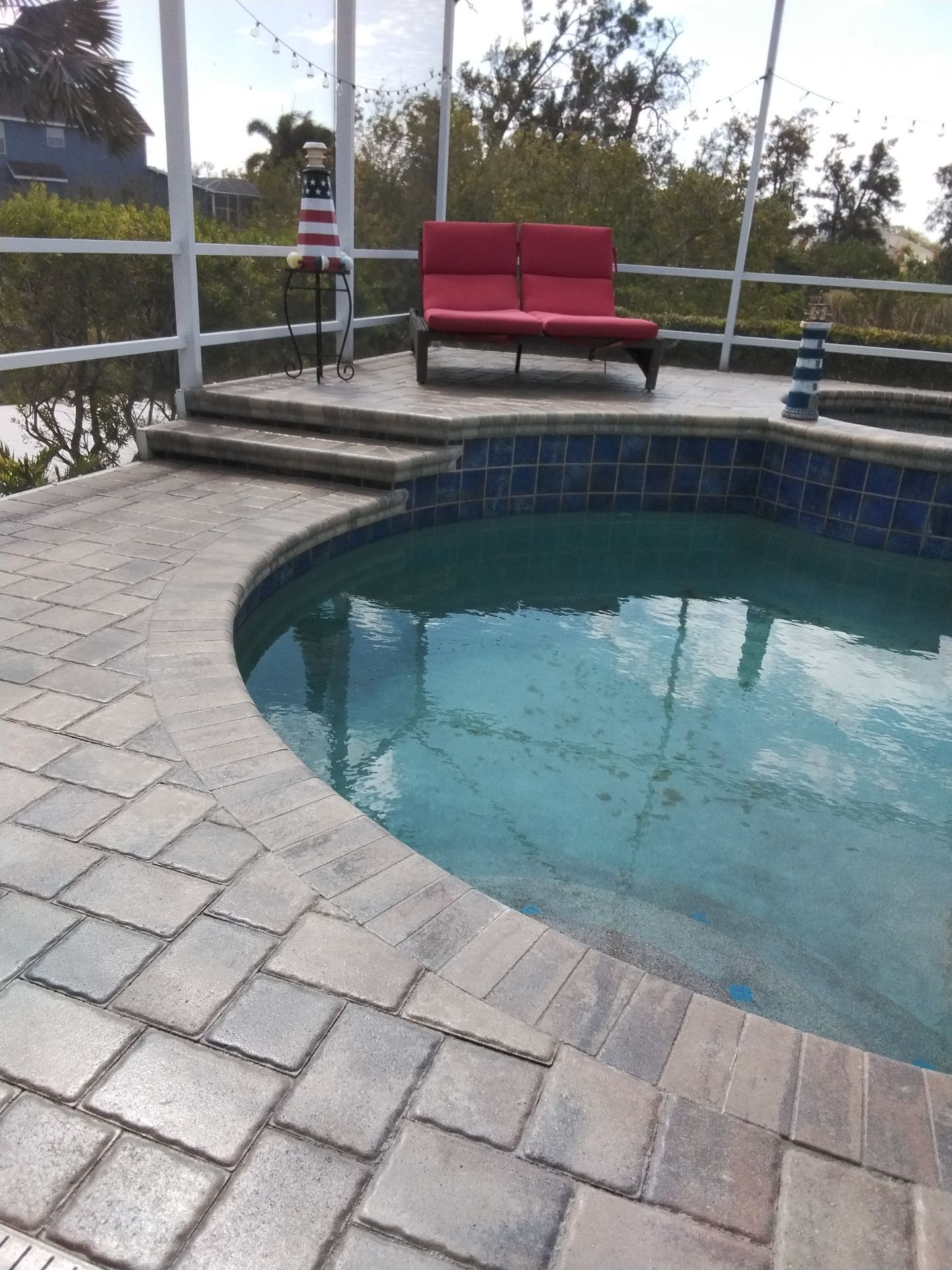 Backyard swimming pool with blue water, stone coping, and a fenced deck with safety signs.
